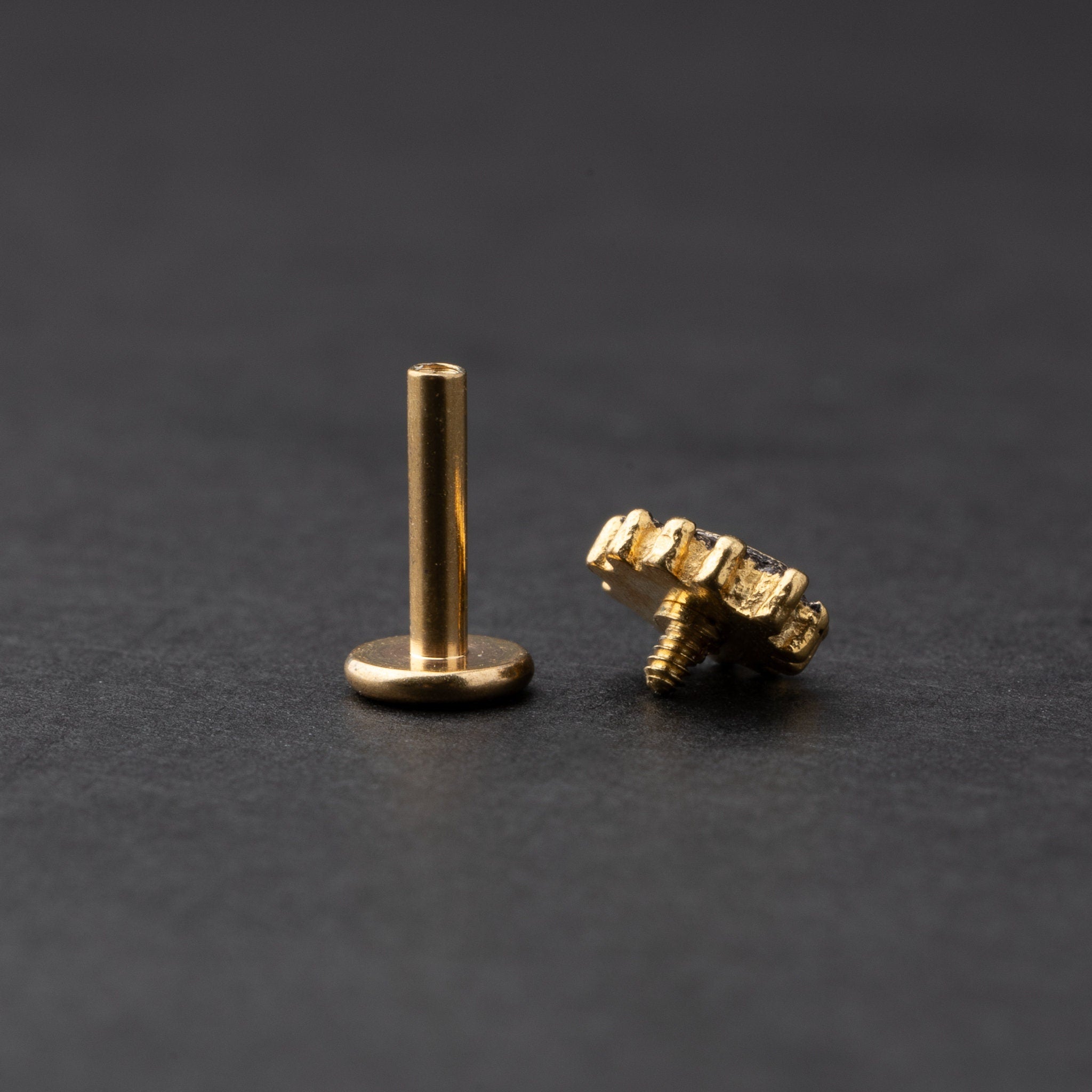 Gold labret stud with a teardrop-shaped crystal centerpiece and detailed border, displayed on a dark background.