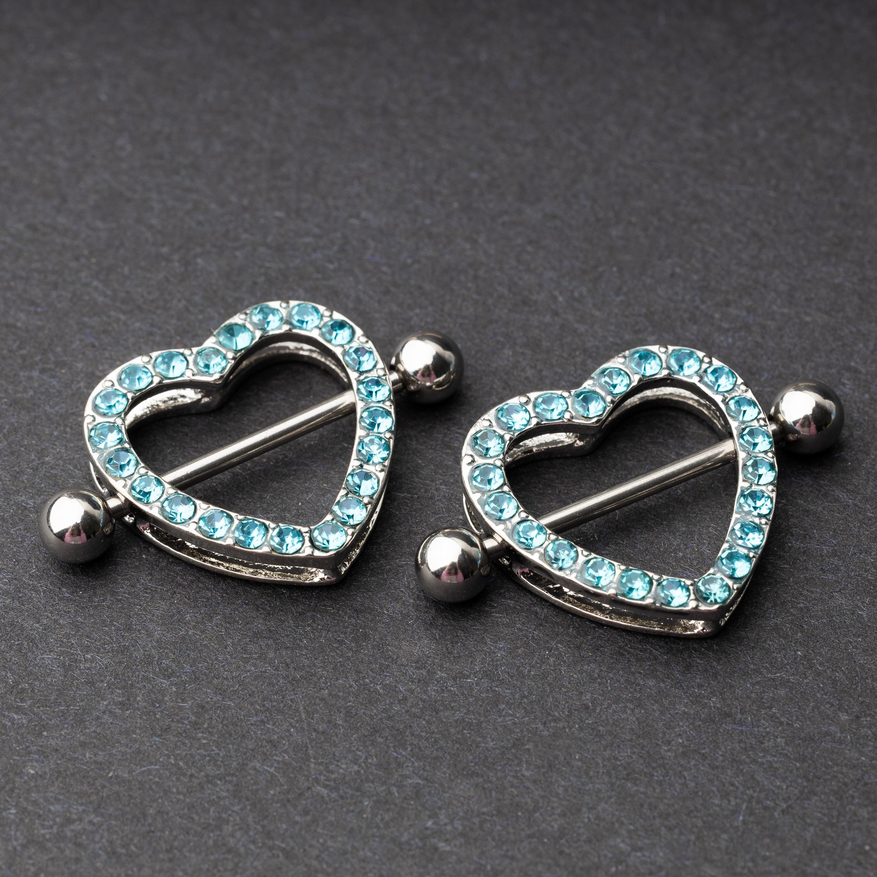Two heart-shaped nipple barbells with silver metal and light blue gemstone accents, displayed on a dark background.