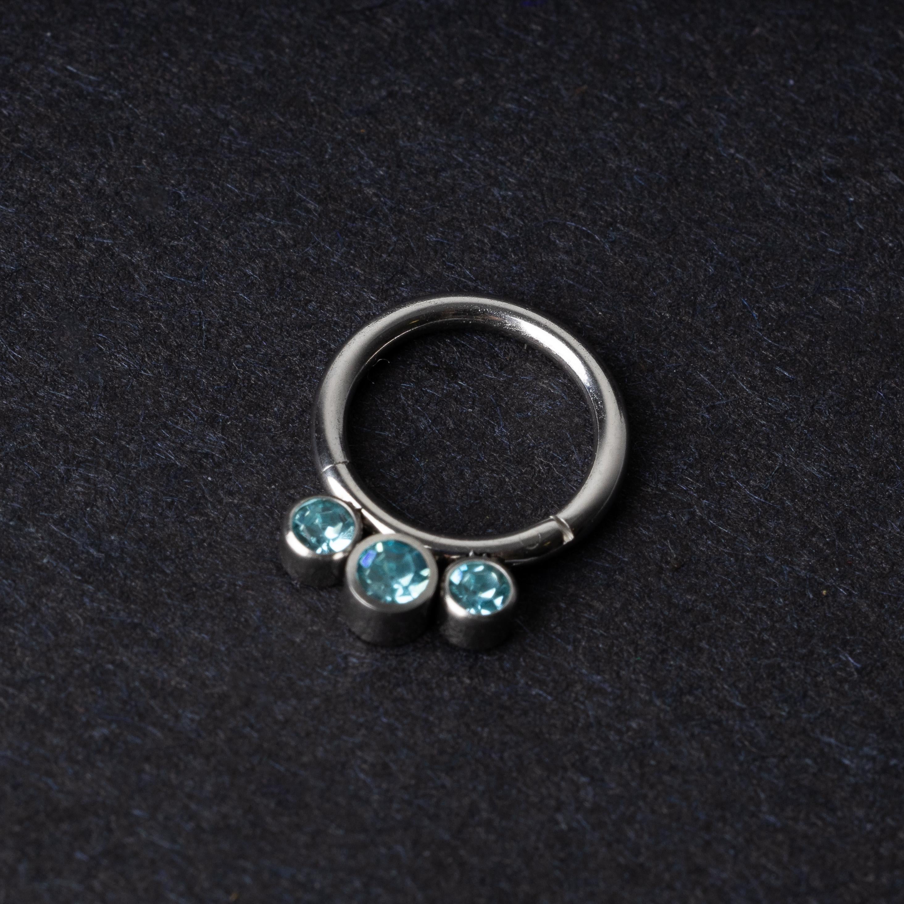 Titanium clicker ring with three aqua-blue gemstones, displayed on a dark background.