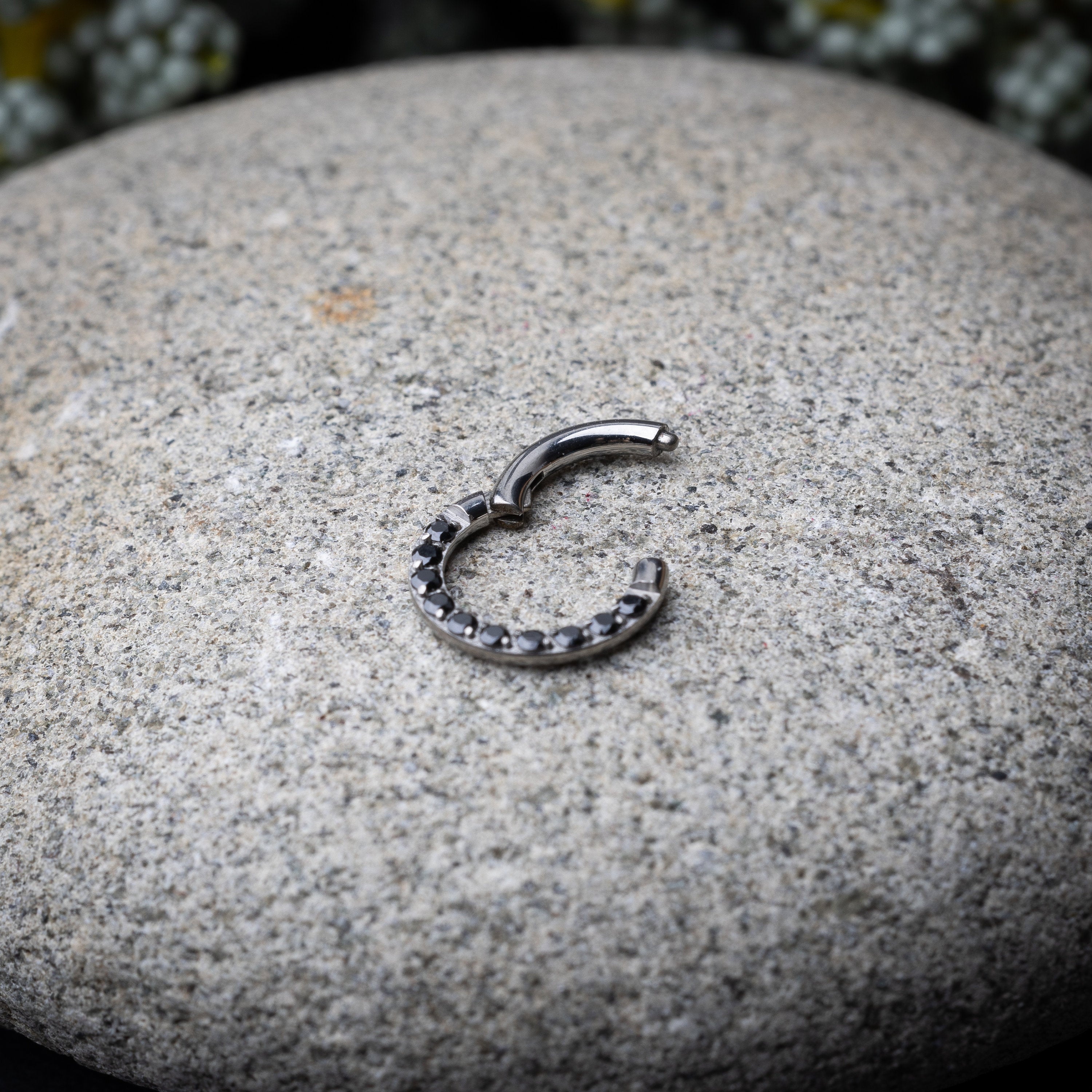 Titanium septum clicker with black gemstones, displayed on a textured dark background.