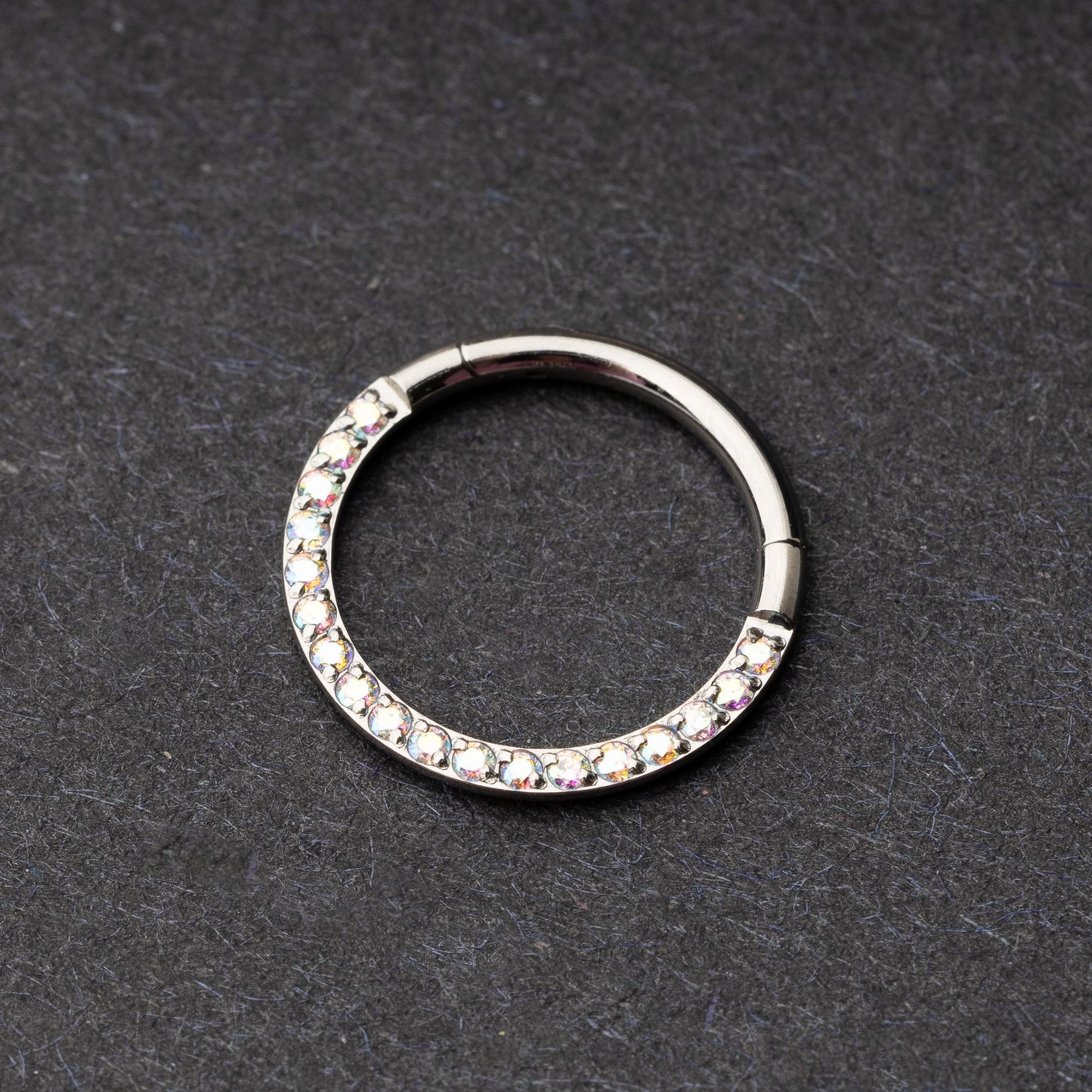 Titanium clicker ring with iridescent crystals, displayed on a dark background.