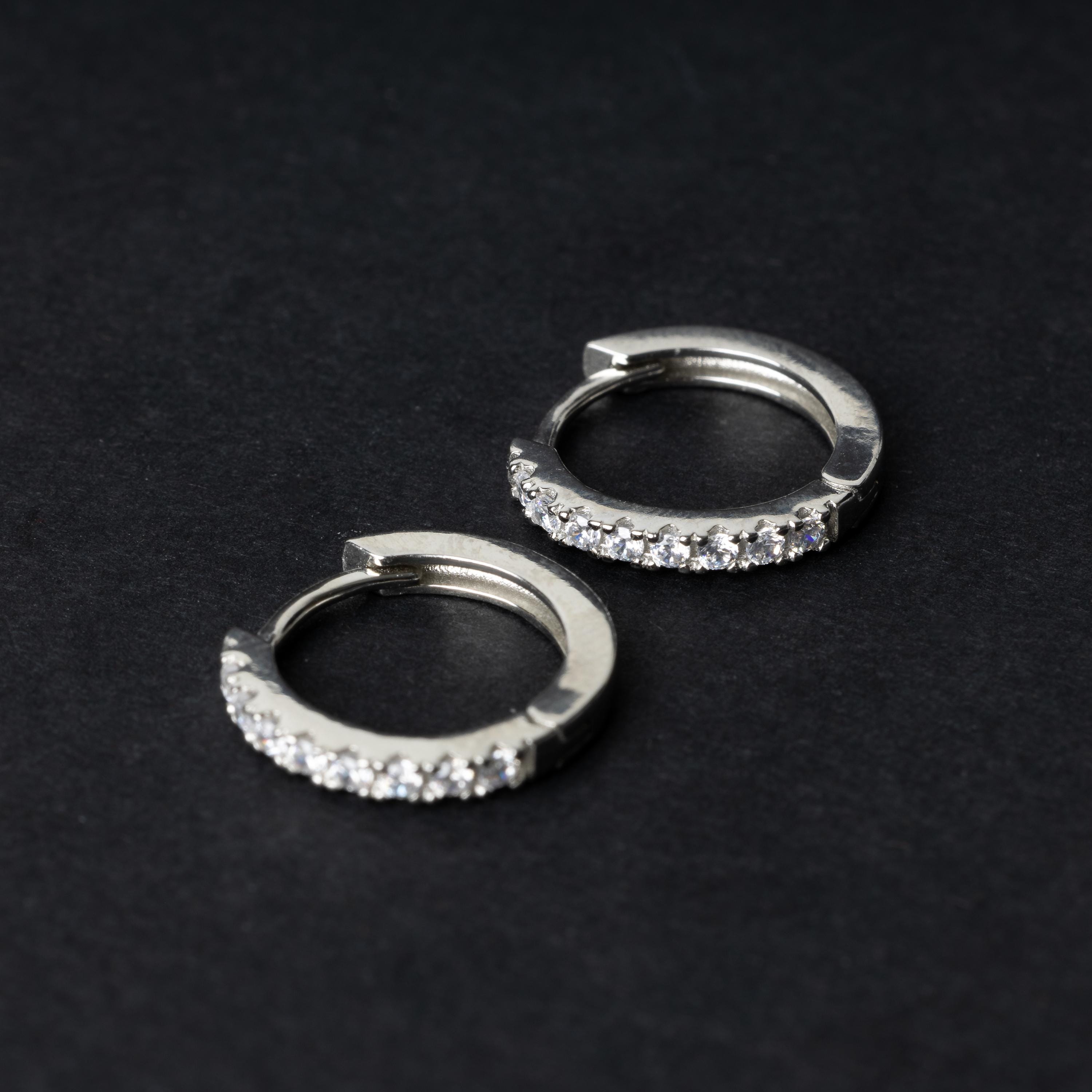 A pair of silver hoop earrings adorned with a row of sparkling cubic zirconia gems, displayed on a black background.