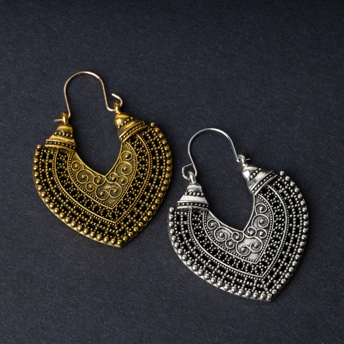 Pair of earrings in antique gold and silver finishes with intricate patterns and textured detailing, displayed on a dark background.