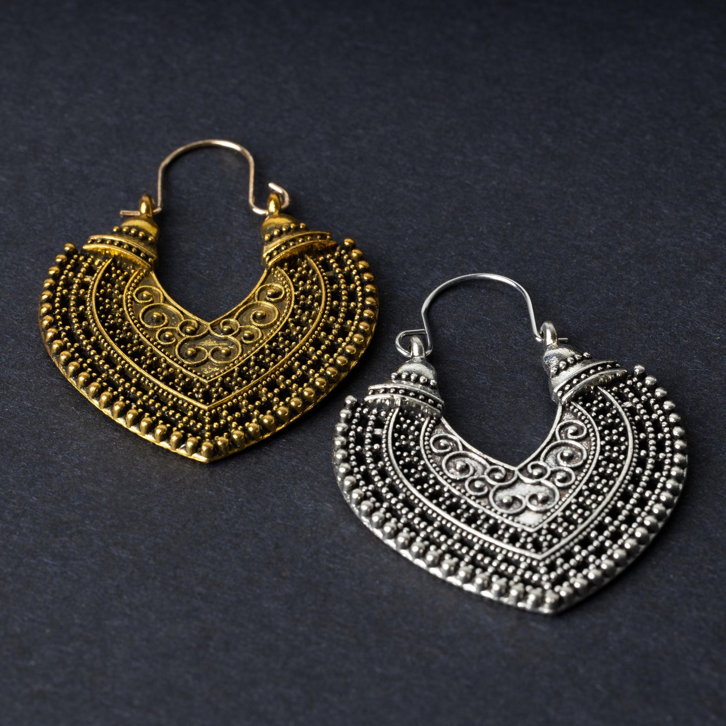 Pair of earrings in antique gold and silver finishes with intricate patterns and textured detailing, displayed on a dark background.