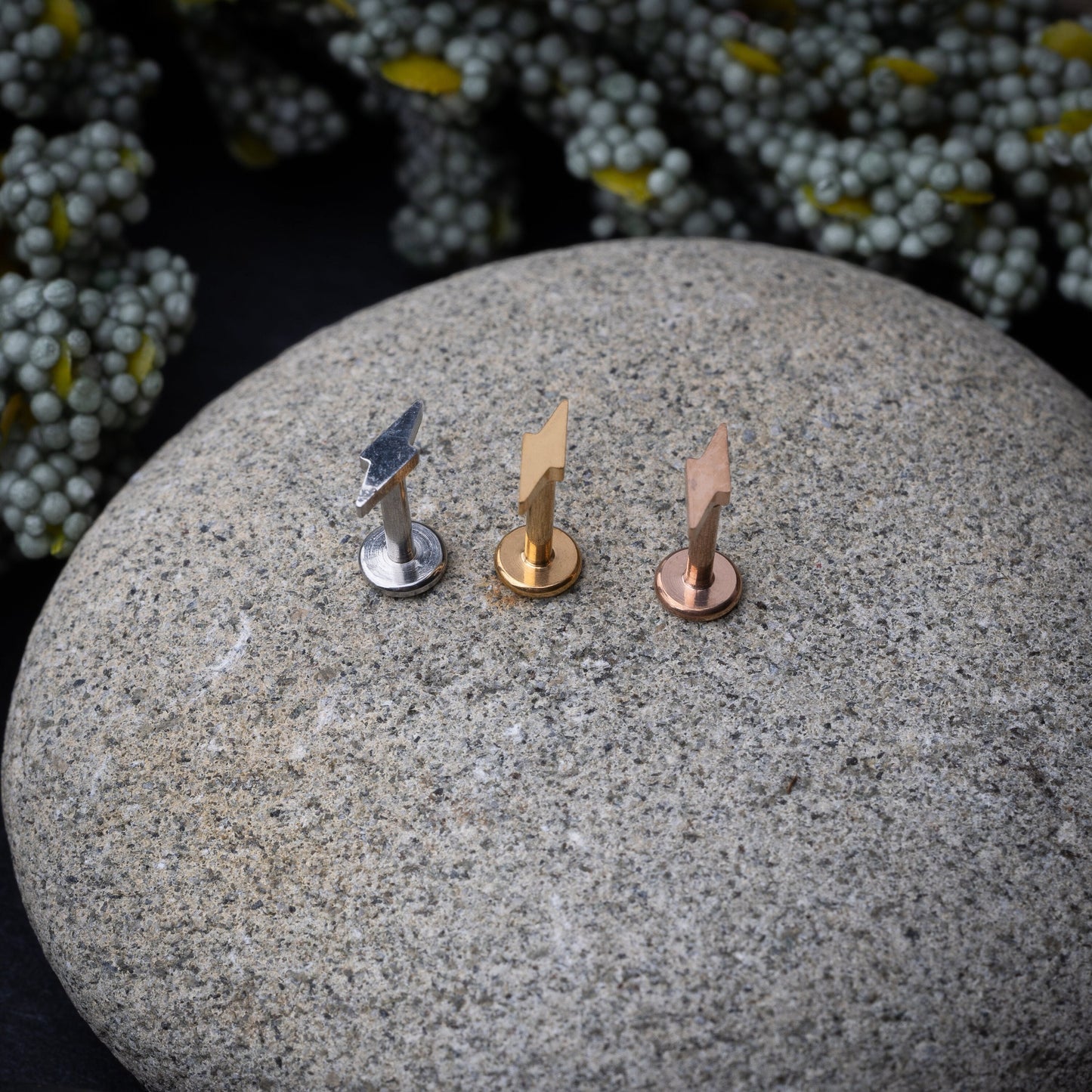 Minimalist lightning bolt labret studs in silver, gold, and rose gold finishes, displayed on a Stone Background