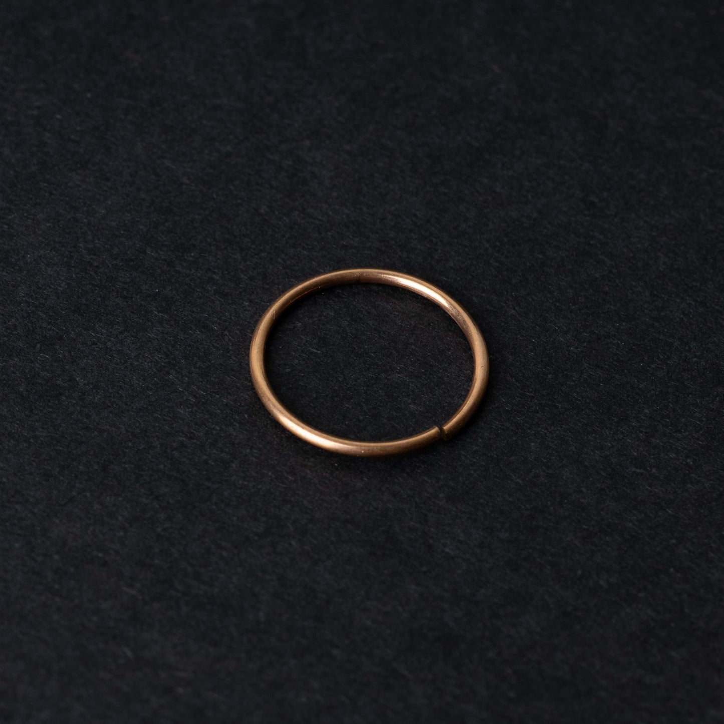 A single thin rose gold seamless hoop with a polished finish, displayed on a dark background.