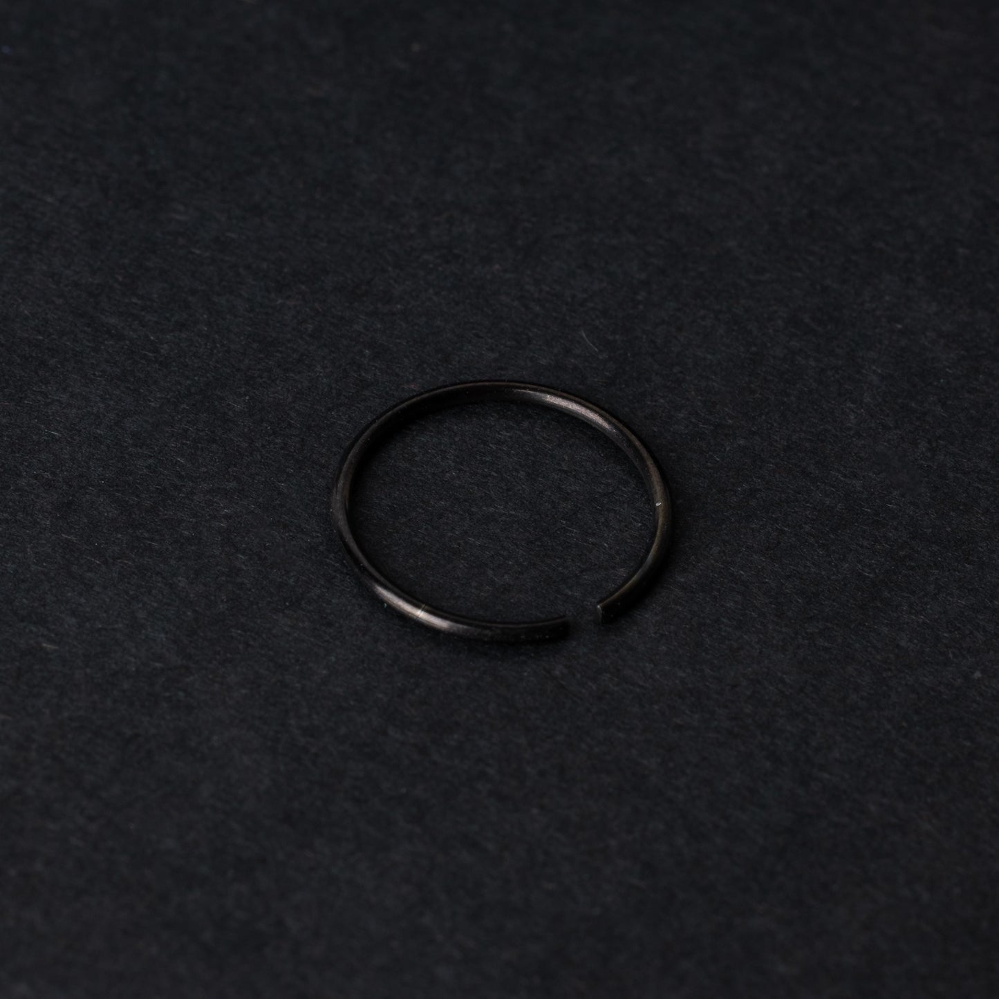 A single thin black seamless hoop with a polished finish, displayed on a dark background.