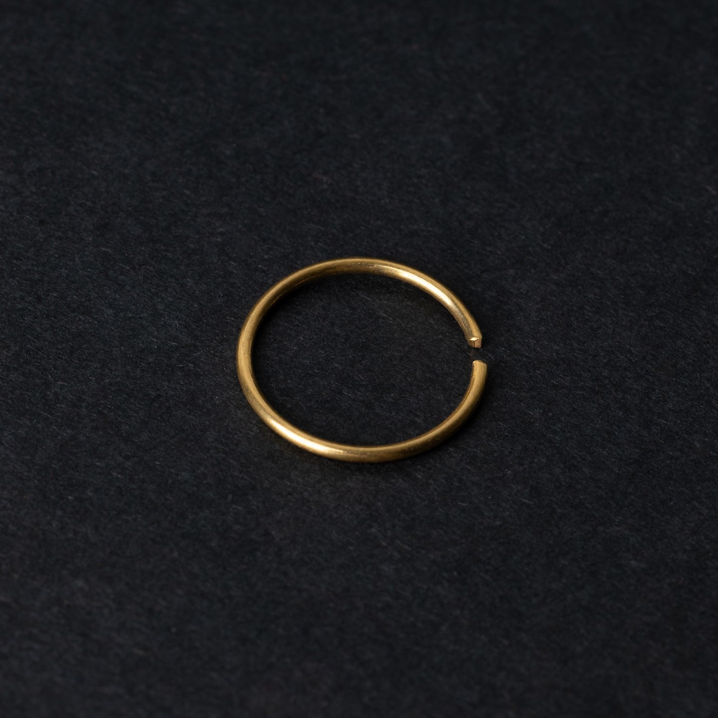 A single thin gold seamless hoop with a polished finish, displayed on a dark background.