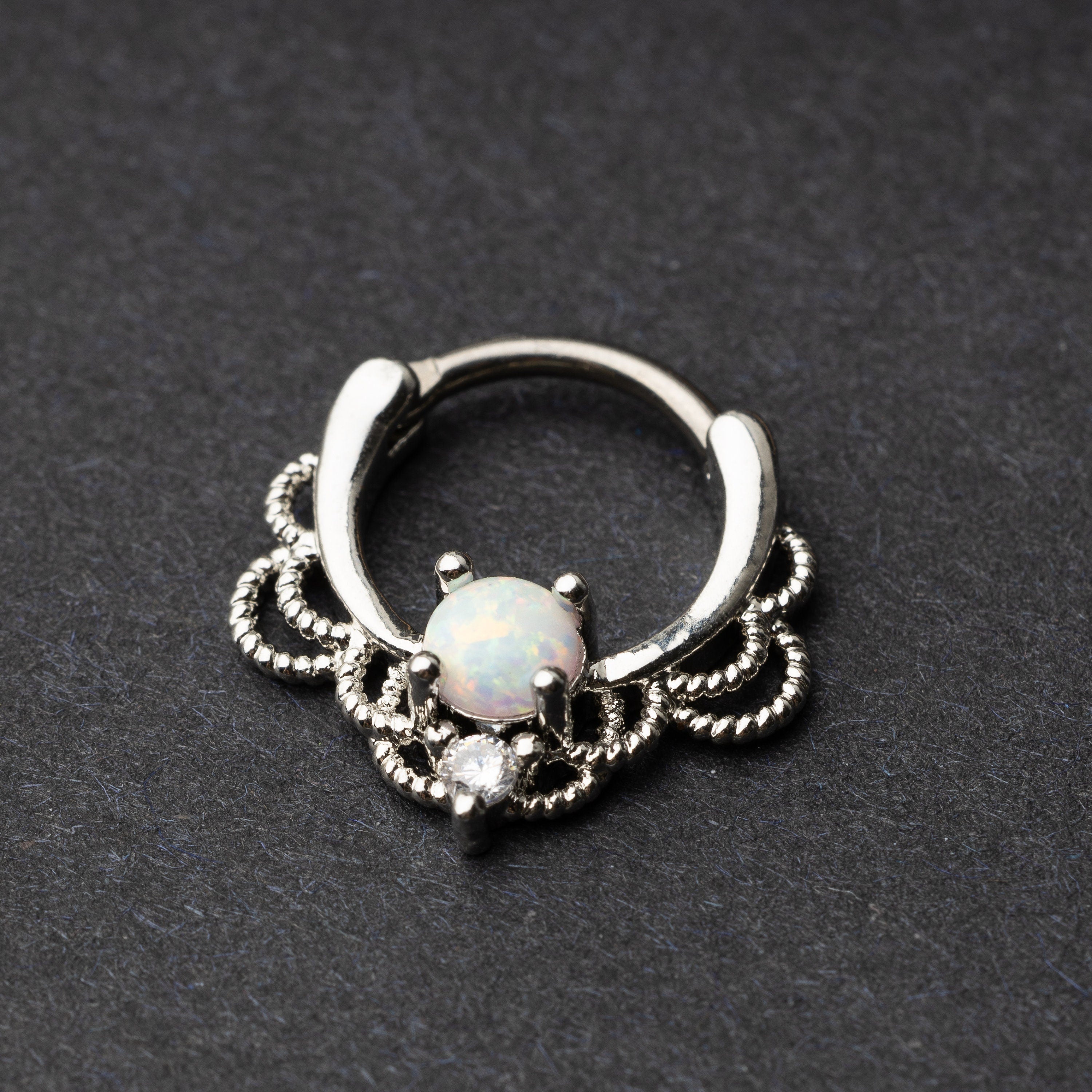 Silver septum clicker with intricate lace design displayed on a dark background.