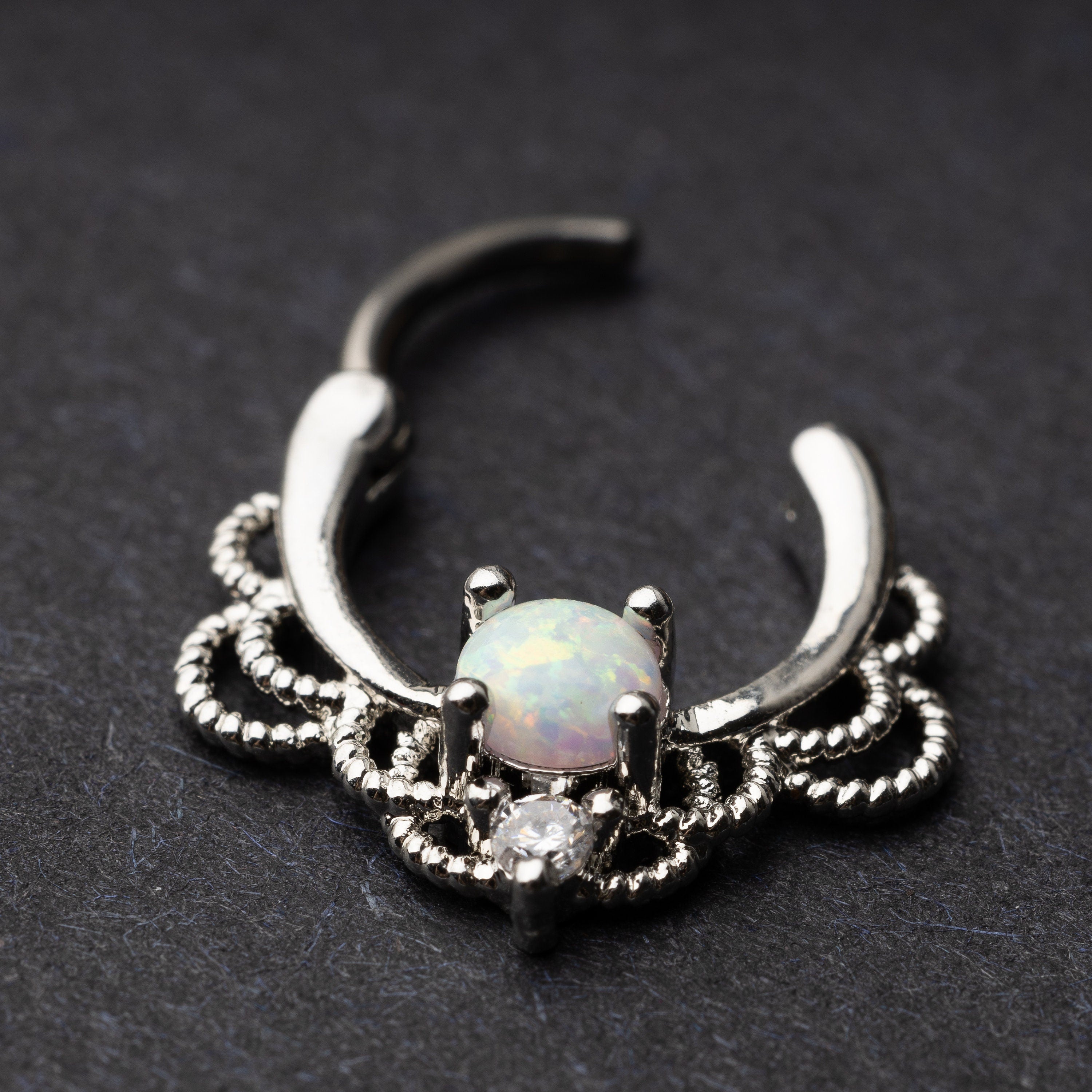 Silver septum clicker with intricate lace design displayed on a dark background.