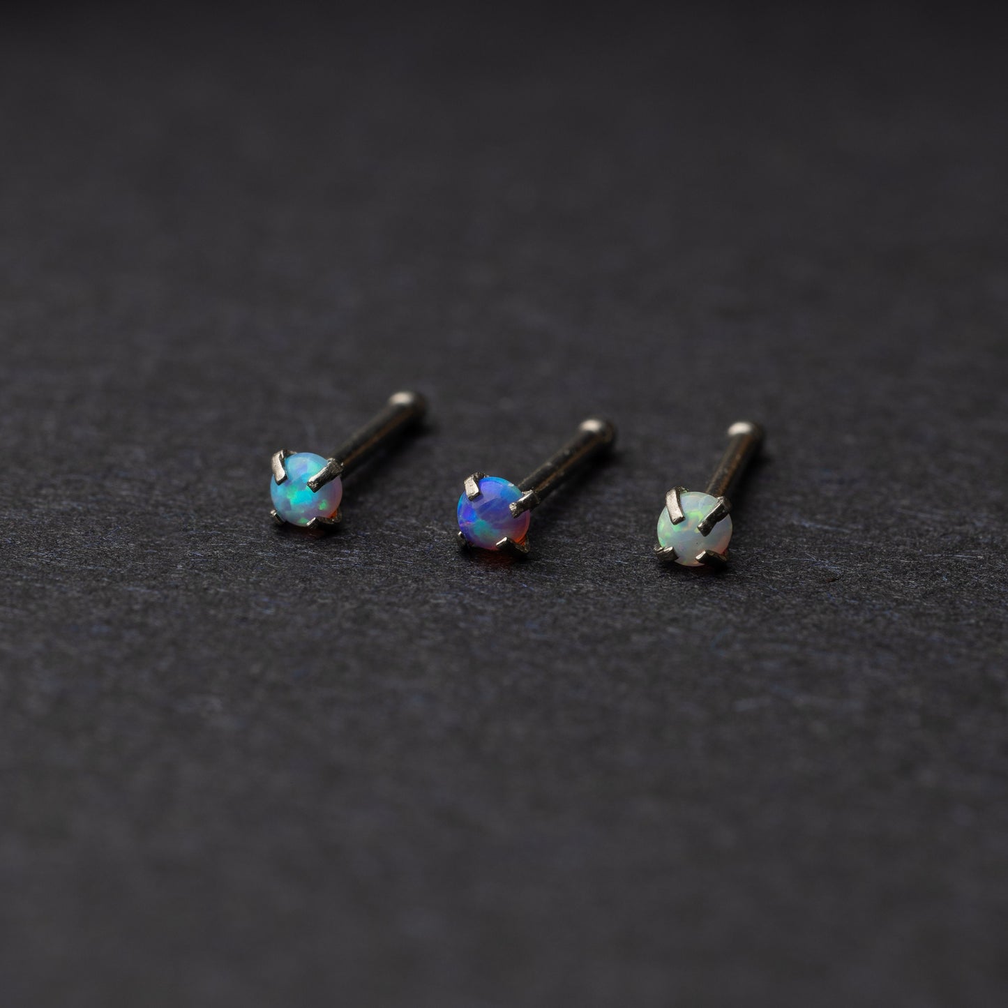 Three opalescent nose studs with prong settings, displayed on a dark background.