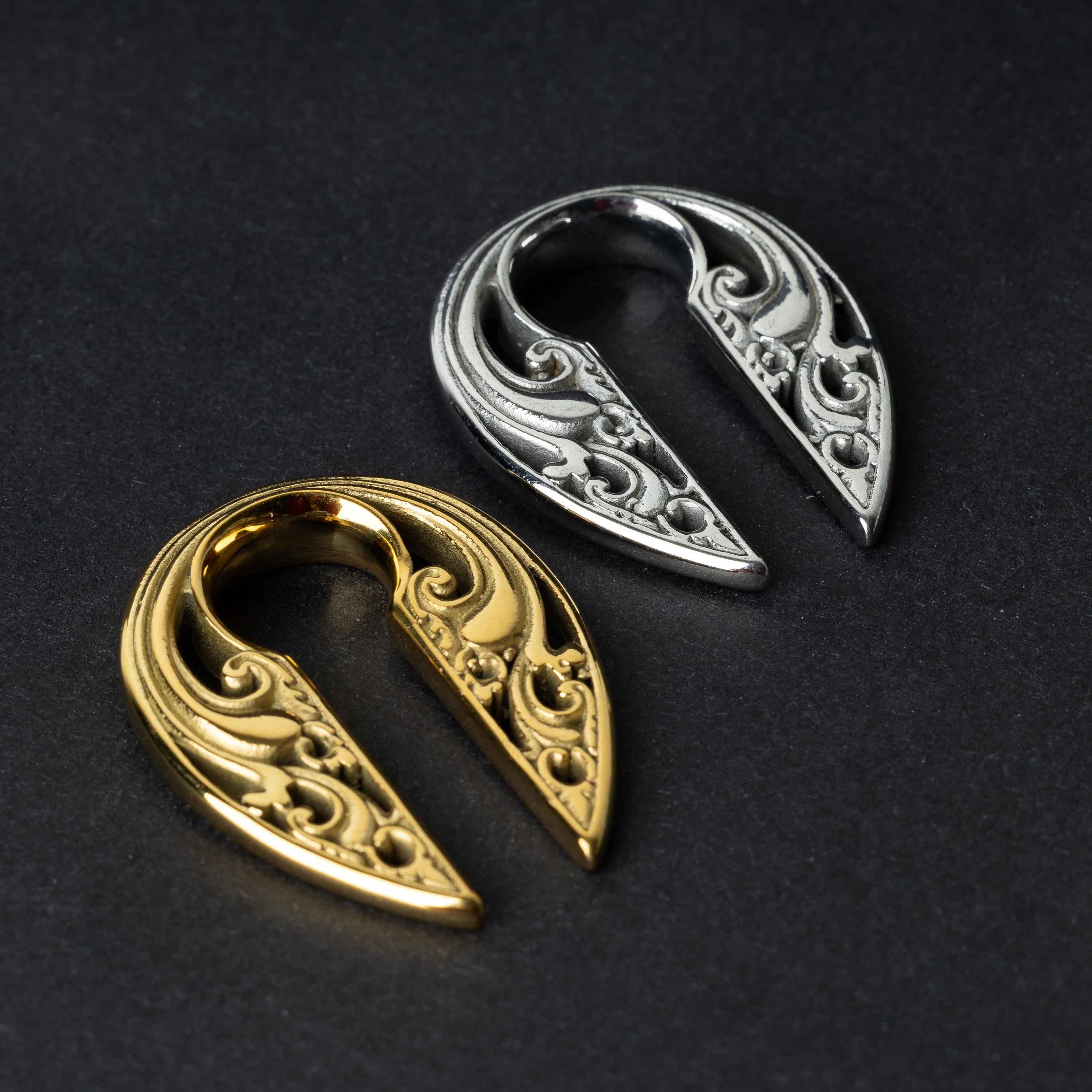Two split ear weights with intricate filigree detailing, one in polished gold and the other in polished silver, displayed on a dark background.