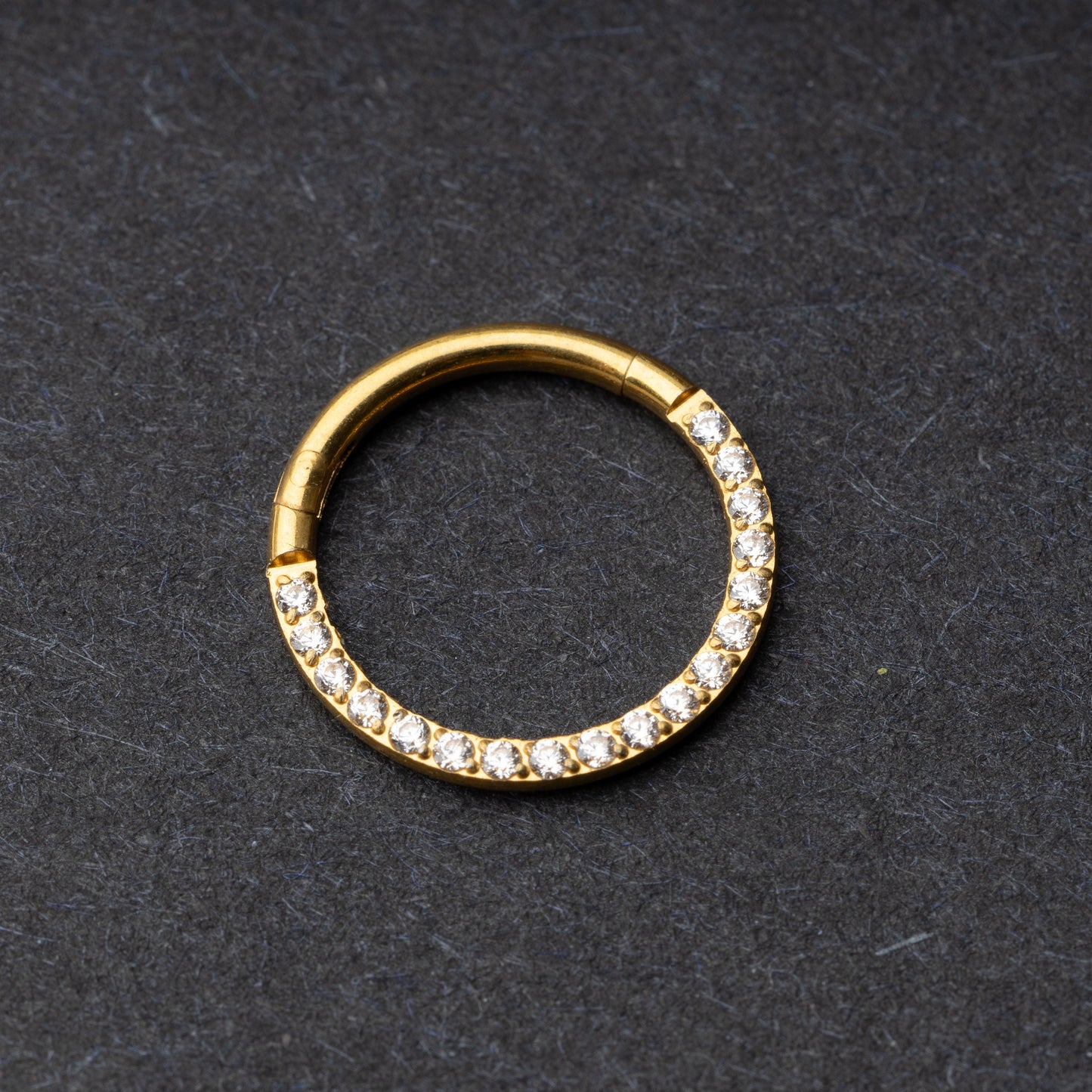 Gold clicker ring with cubic zirconia accents, displayed on a dark background.