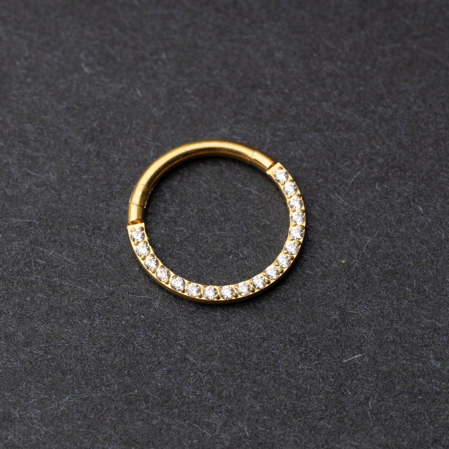 Gold clicker ring with cubic zirconia accents, displayed on a dark background.