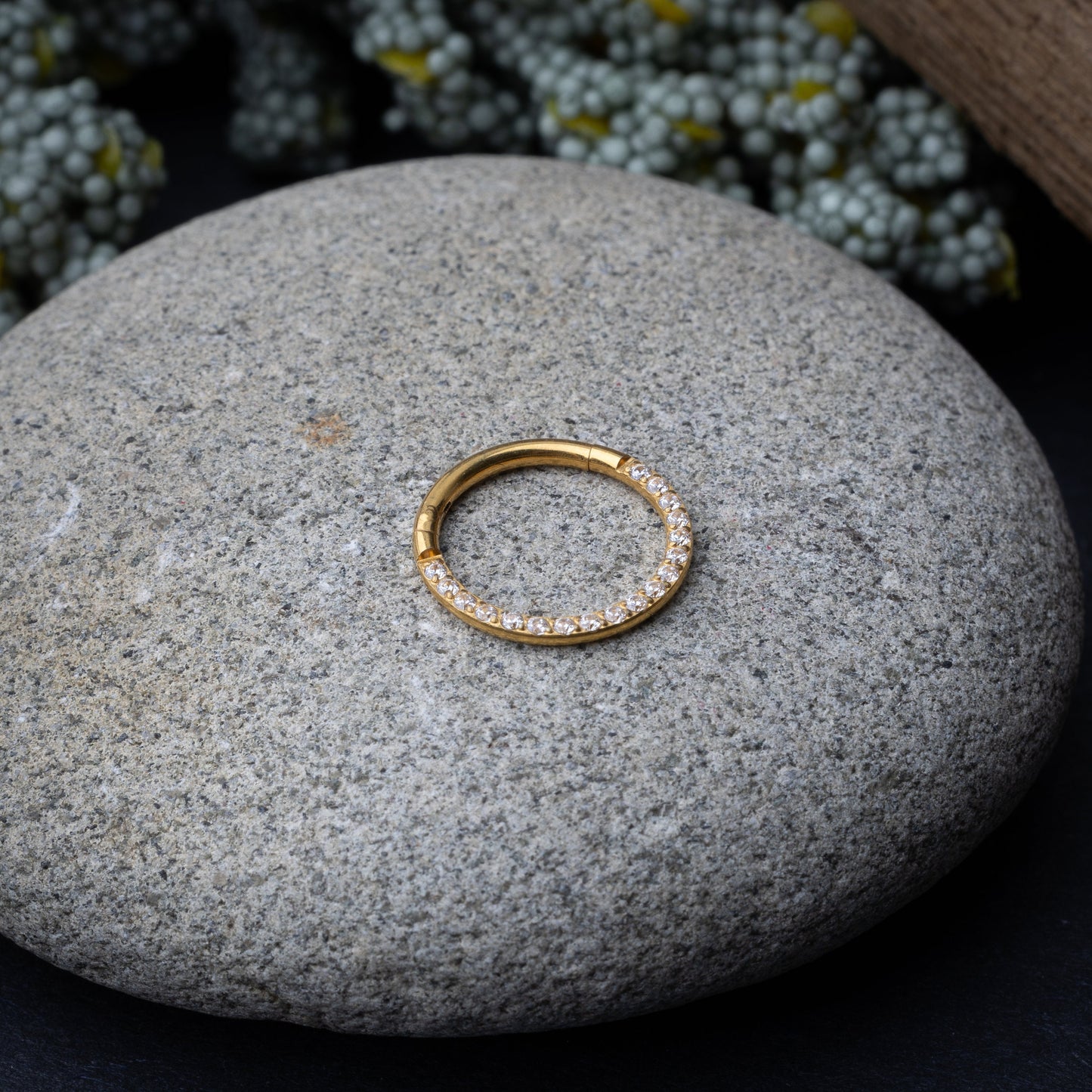 Gold clicker ring with cubic zirconia accents, displayed on a stone background.