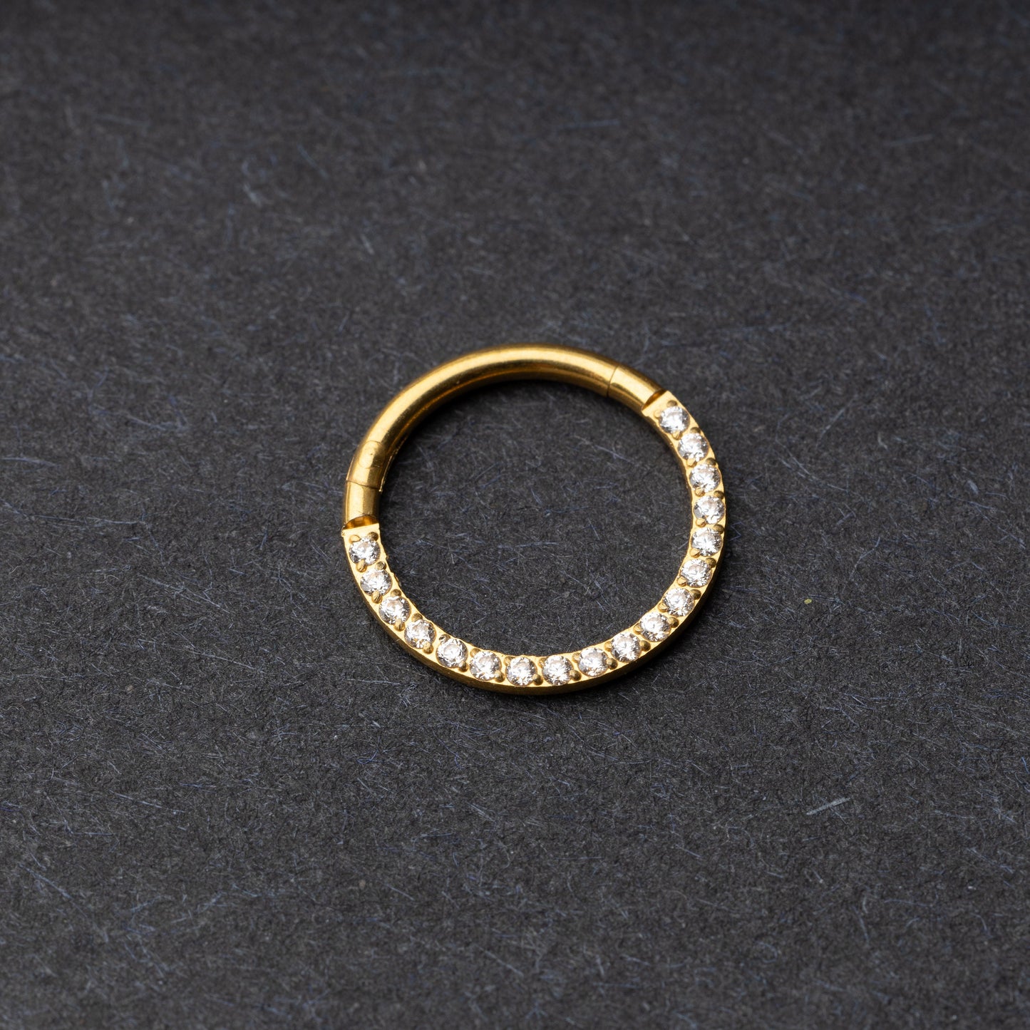Gold clicker ring with cubic zirconia accents, displayed on a dark background.