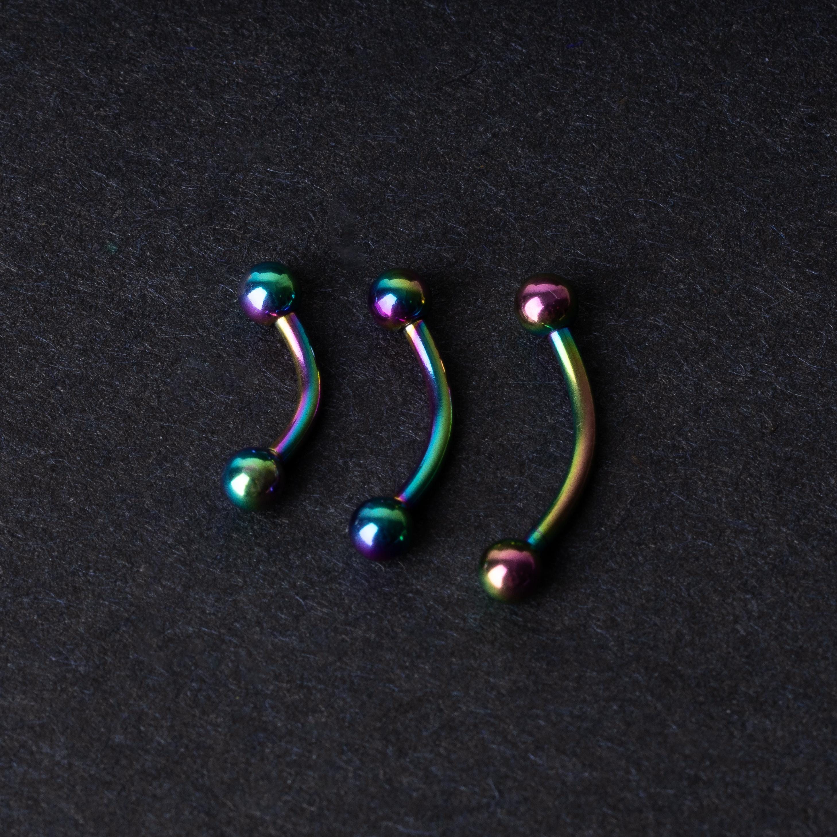 Three curved titanium barbells with a rainbow iridescent finish displayed on a dark textured background, highlighting their vivid colors and smooth finish.