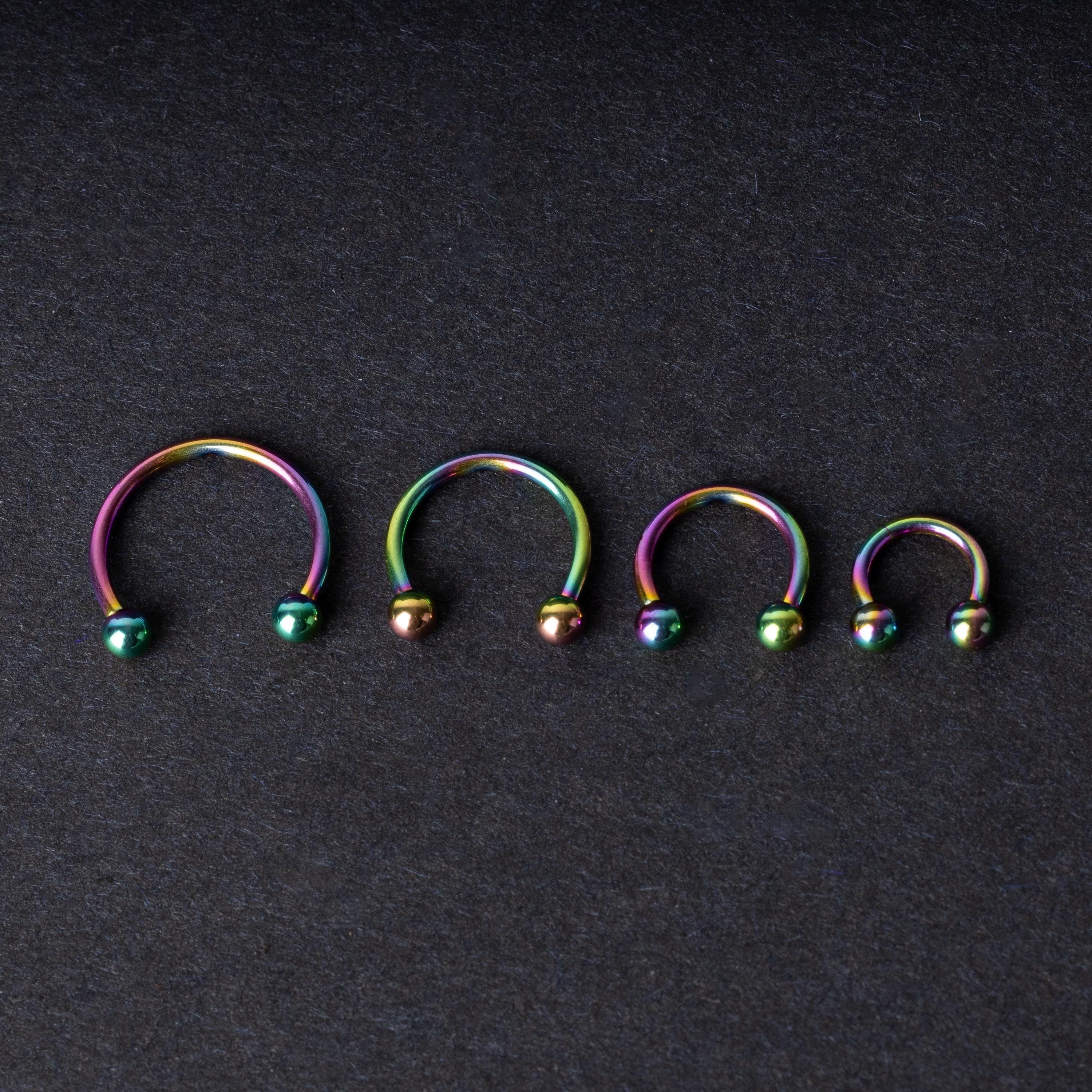 Close-up of four anodized rainbow horseshoe rings in varying sizes, with vibrant, multicolor finishes, displayed on a dark background.