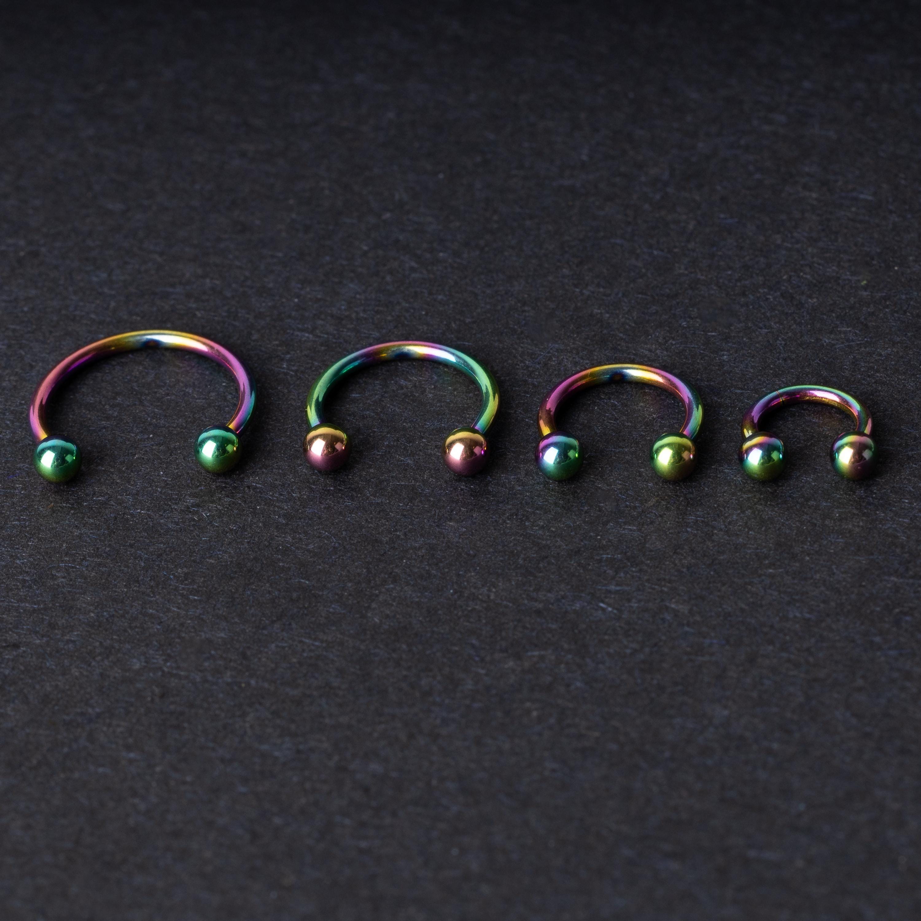 Close-up of four anodized rainbow horseshoe rings in varying sizes, with vibrant, multicolor finishes, displayed on a dark background.
