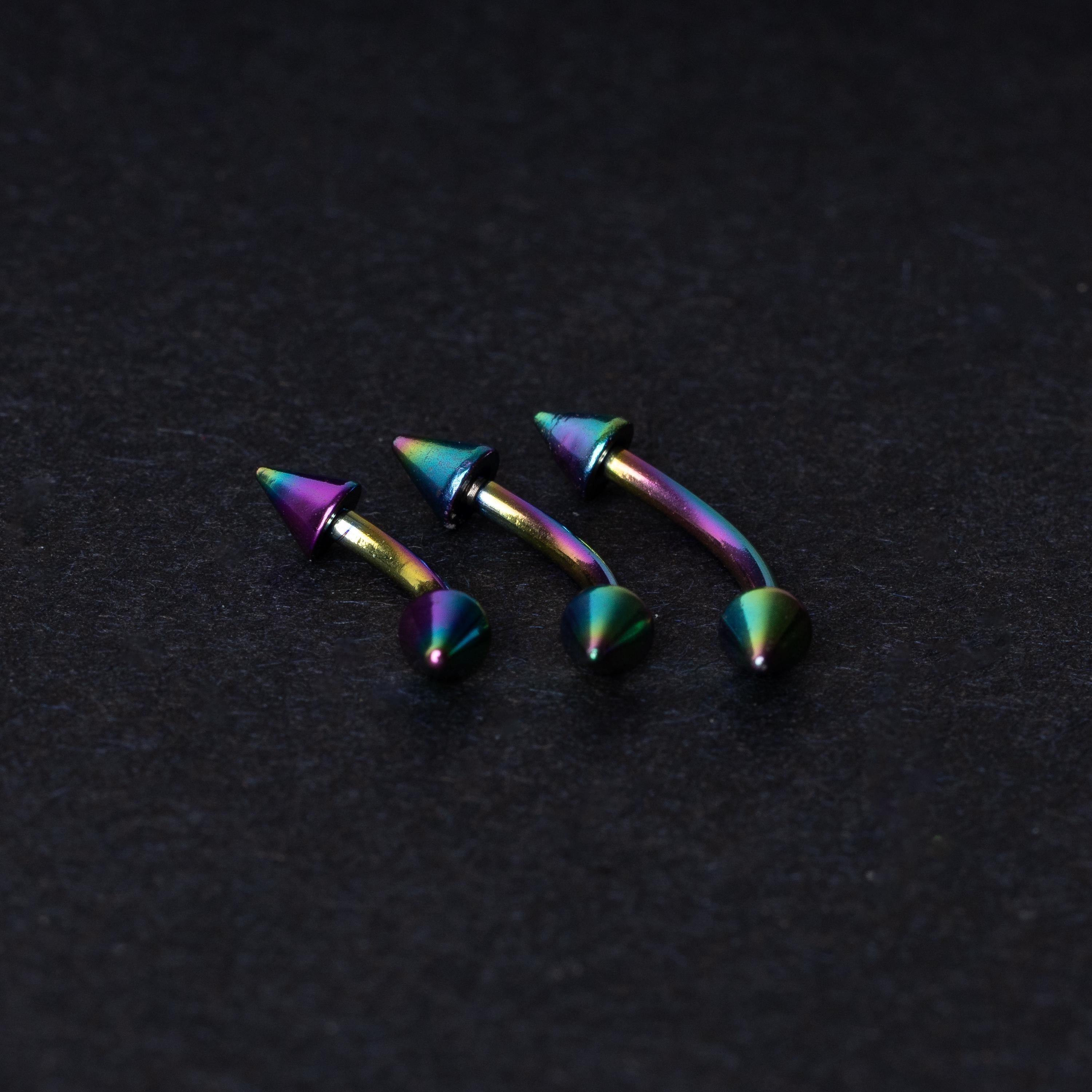 Three rainbow titanium curved barbells with cone-shaped ends, displayed on a dark textured background, showcasing their vivid color gradient and sleek design.
