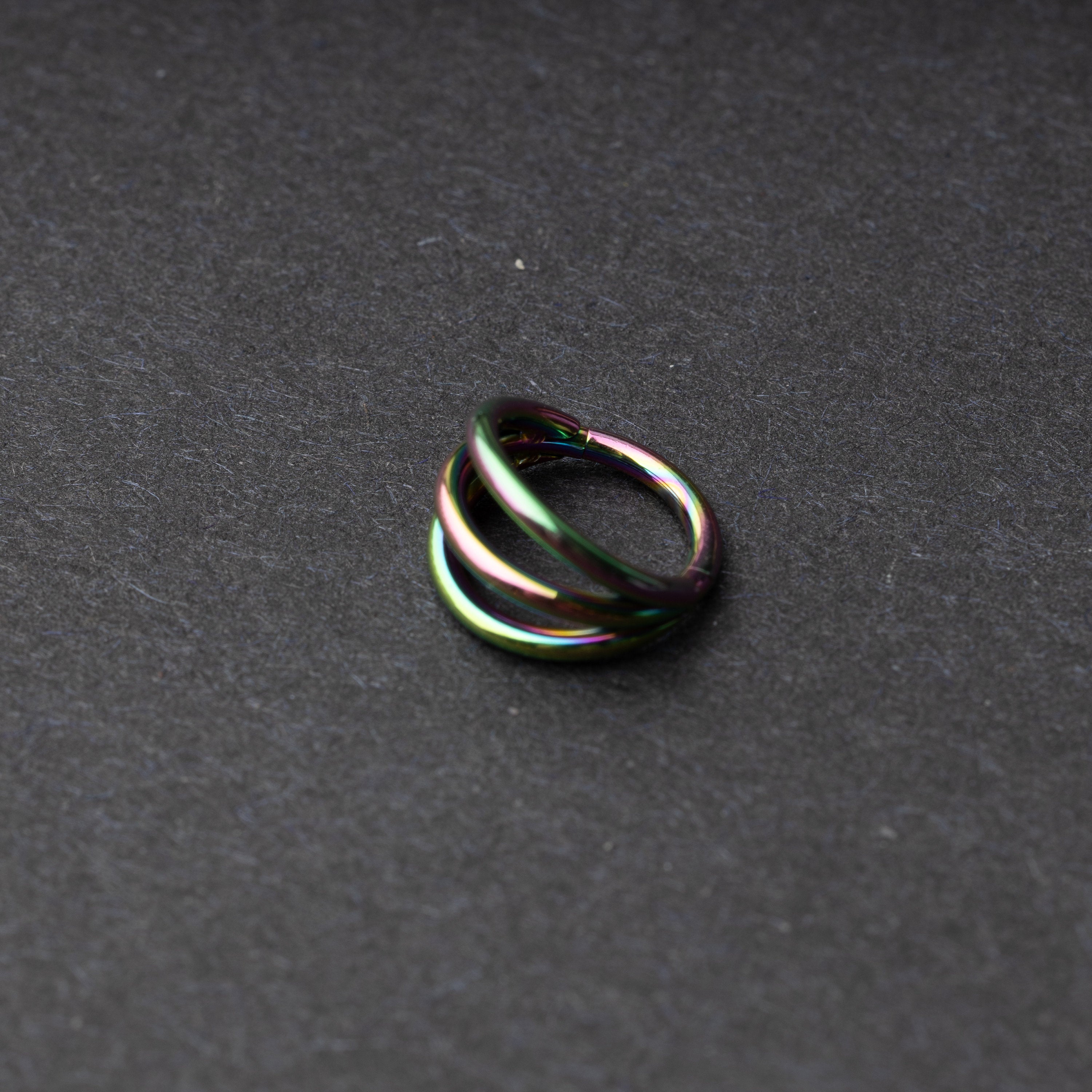 Four triple-band hoop septum clicker ring in rainbow finish, displayed on a dark background.