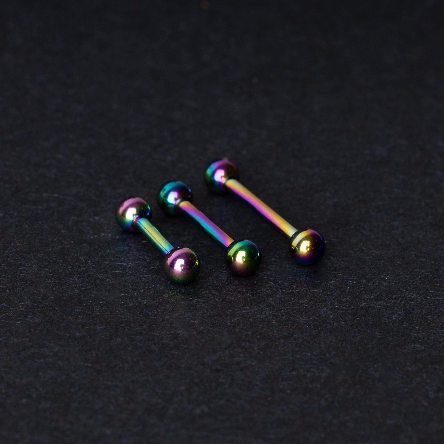 Rainbow stainless steel barbells with an anodized finish on a dark background.