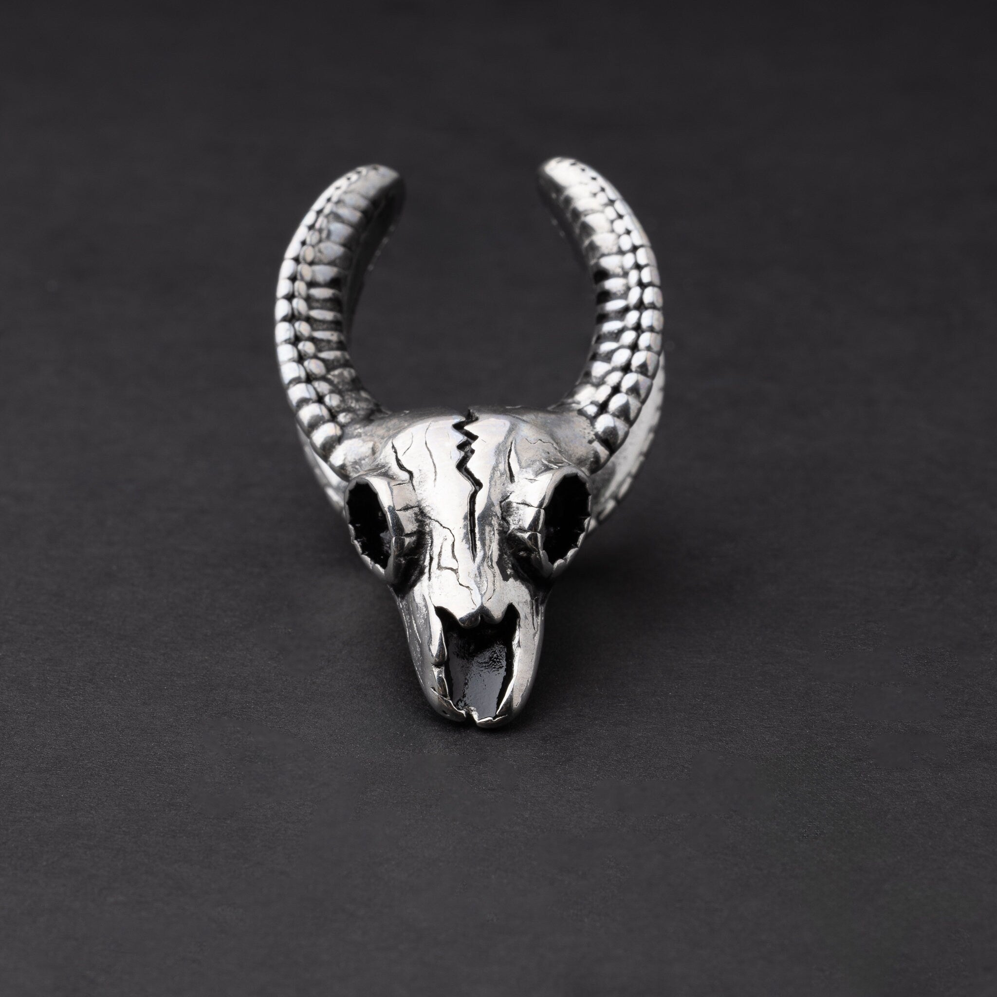 Ram skull saddle tunnel in silver, showcasing intricate skull details and bold design on a dark background.