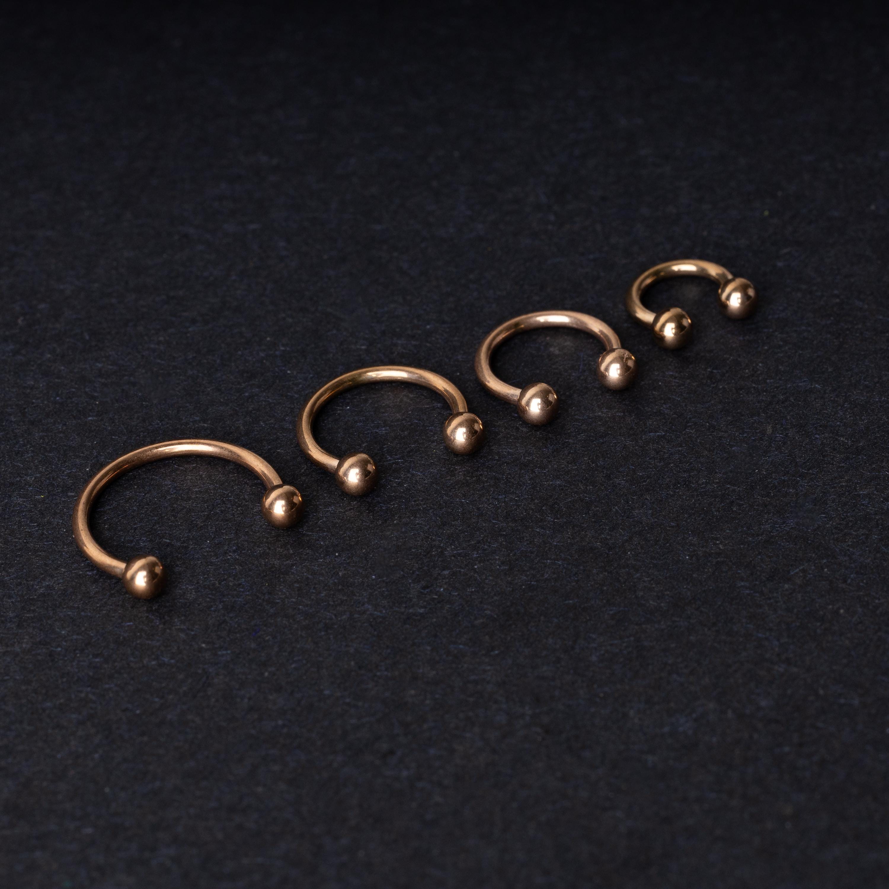 Rose Gold-tone horseshoe rings displayed in a row on a dark background, showcasing various sizes for septum or body piercings.