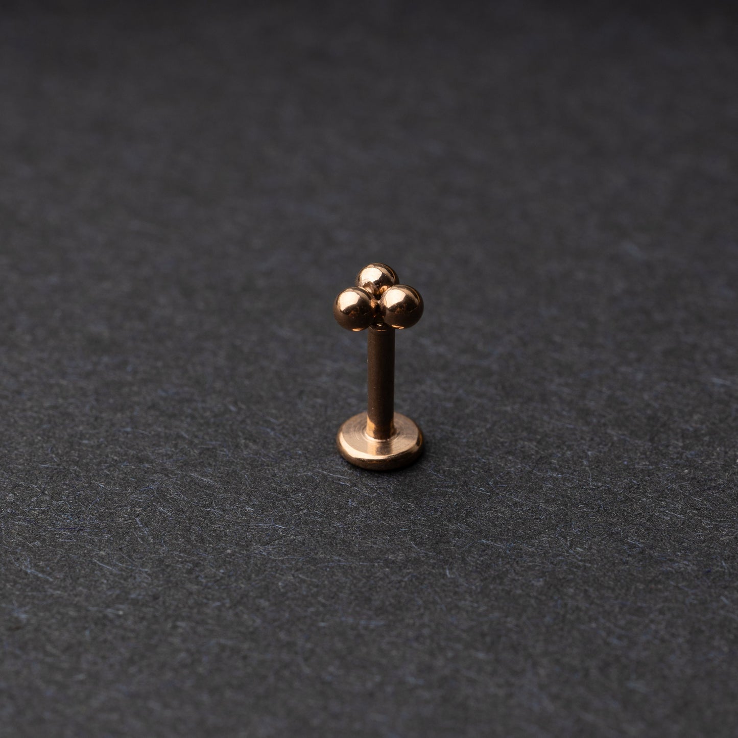 Close-up of three minimalist ball cluster labret studs in a rose gold finish, displayed on a dark background.