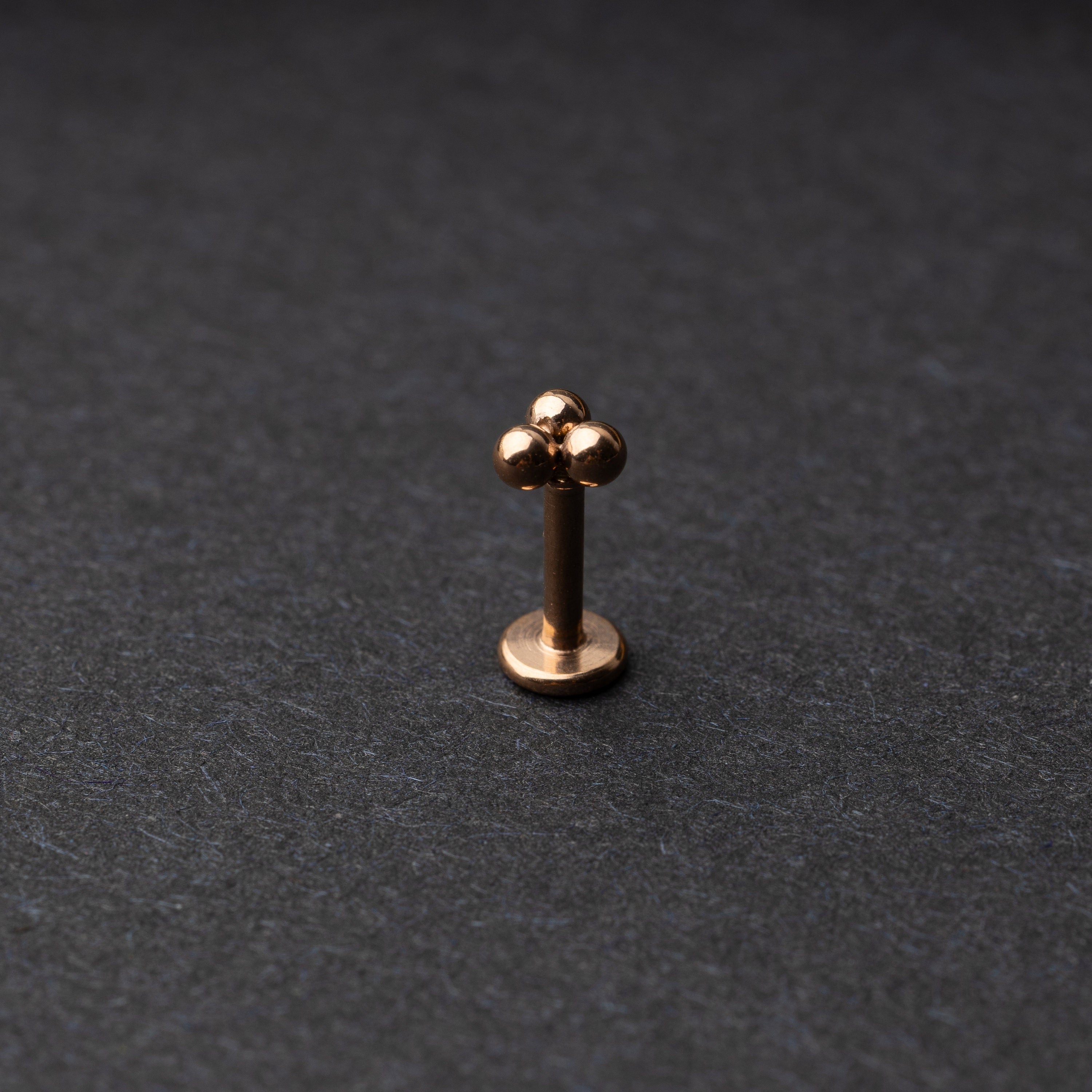 Close-up of three minimalist ball cluster labret studs in a rose gold finish, displayed on a dark background.