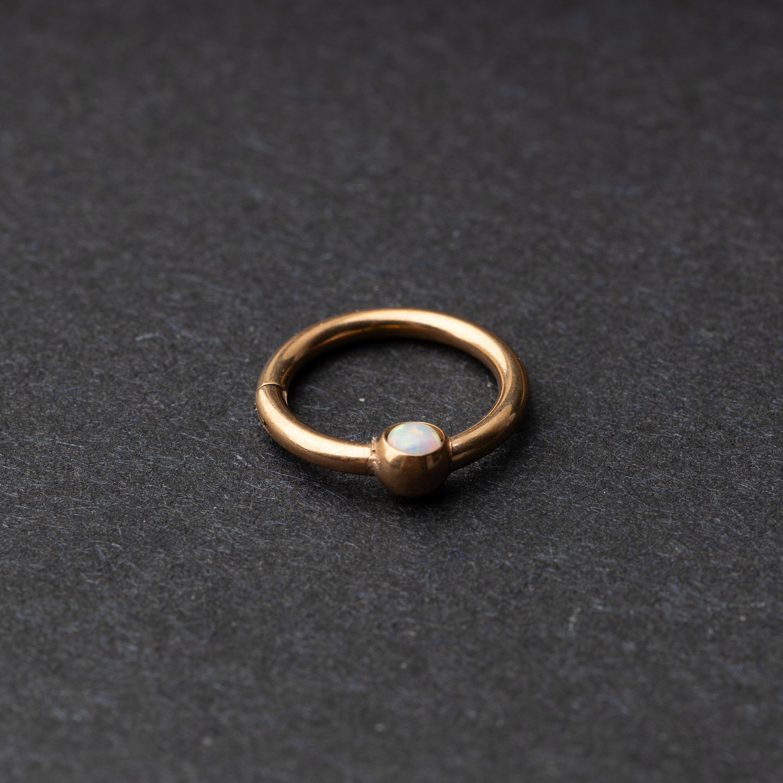 Seamless clicker in rose gold featuring an opalescent bead, displayed on a dark background.