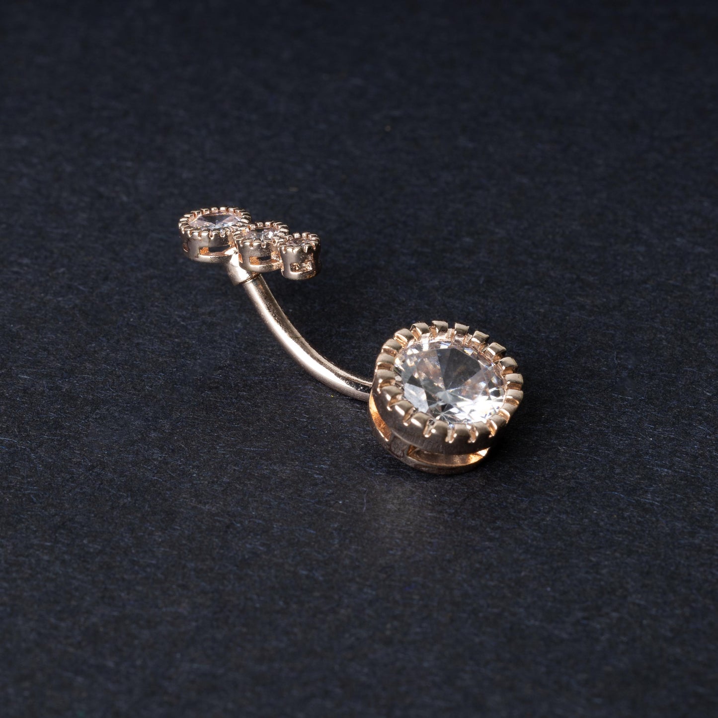 Double-jeweled belly rings in rose gold with large and small crystal accents, displayed on a dark background.