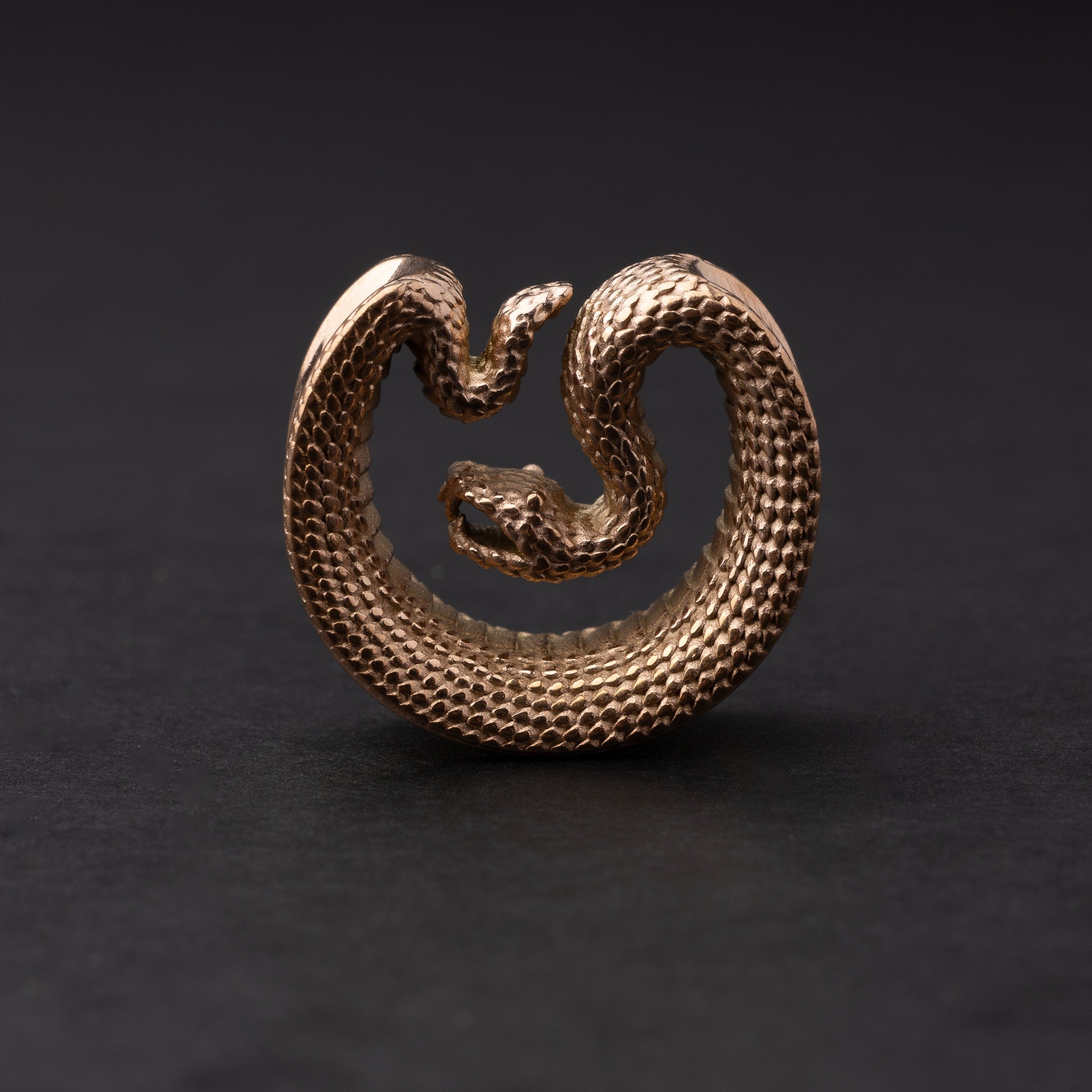 Rose Gold Gold Snake-shaped saddle plugs, displayed on a dark background.