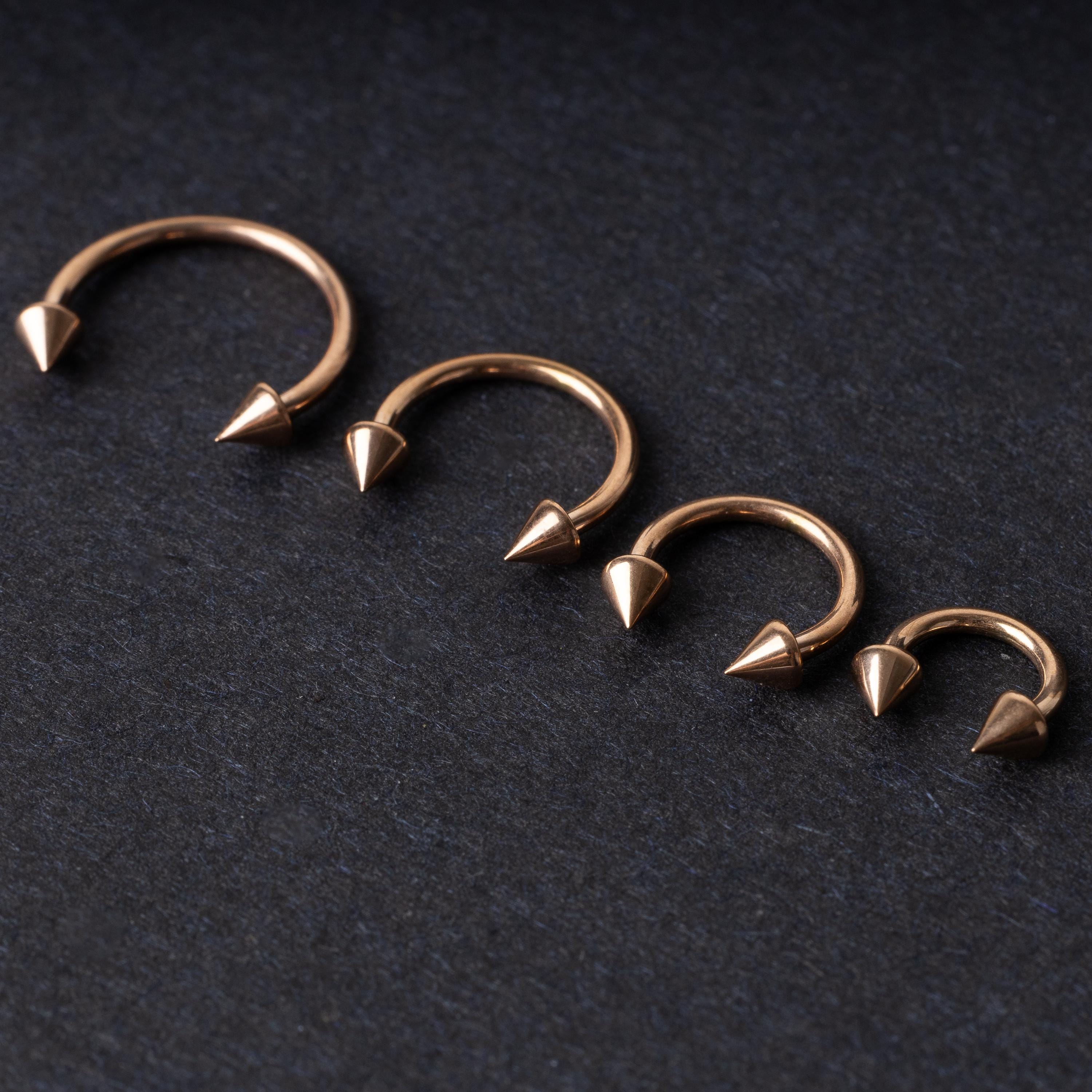 Four rose gold-tone horseshoe hoops with spike ends, arranged in descending size order on a dark textured background.