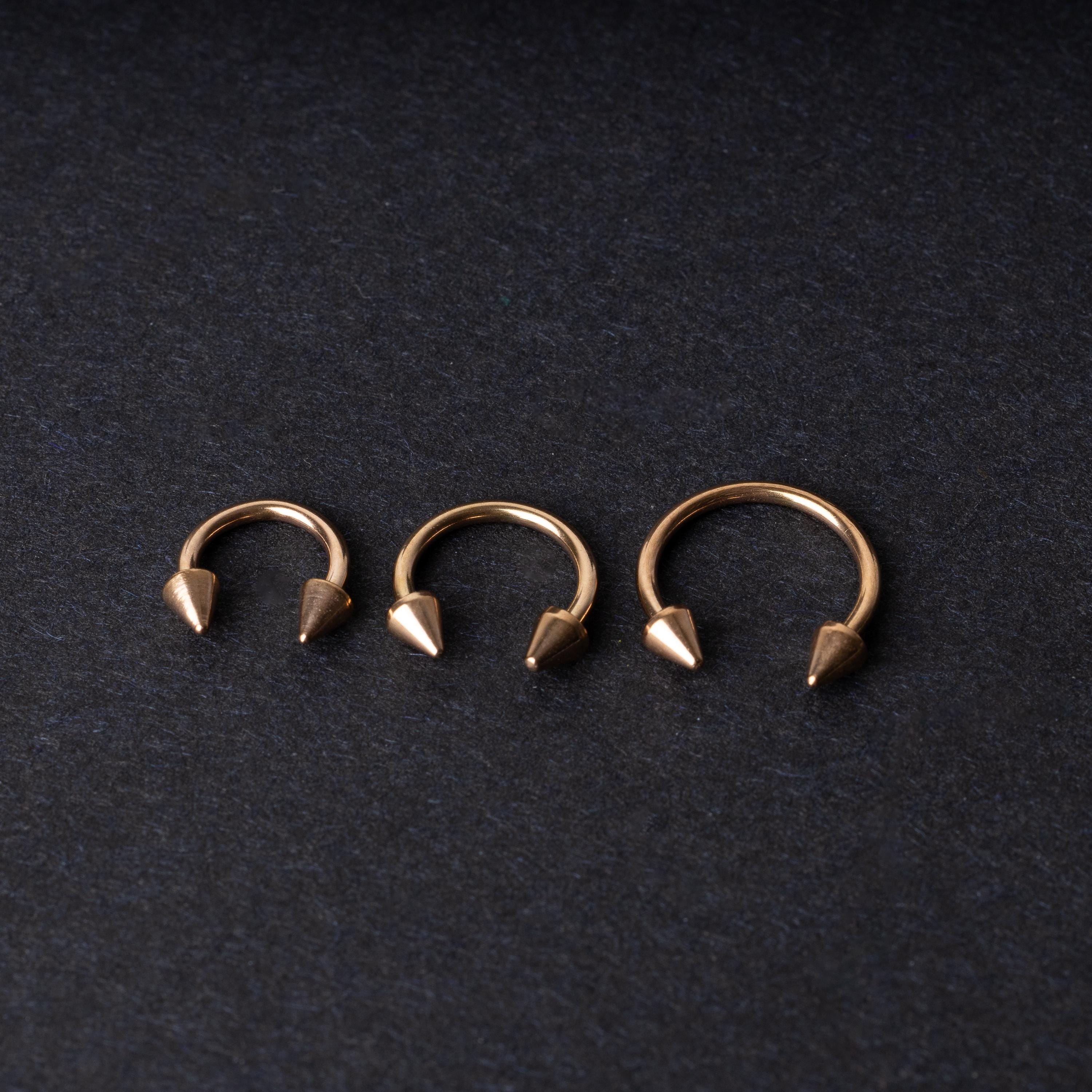 Three rose gold-tone horseshoe hoops with threaded spike ends arranged on a dark textured background.