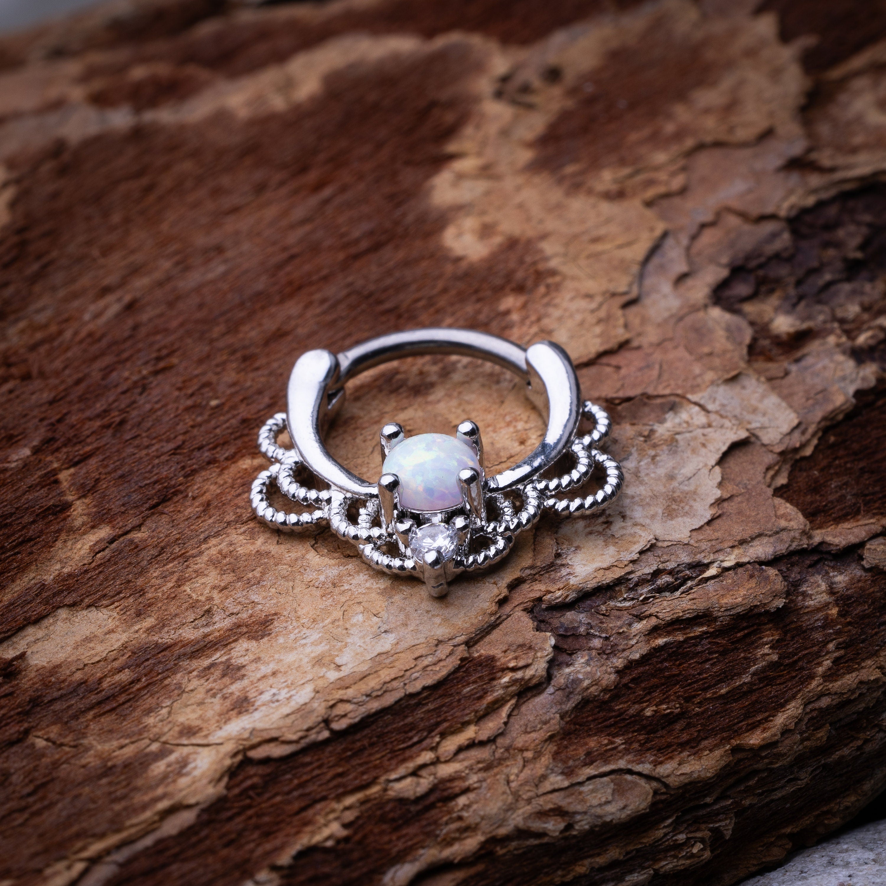Silver septum clicker with intricate lace design displayed on a wooden background.