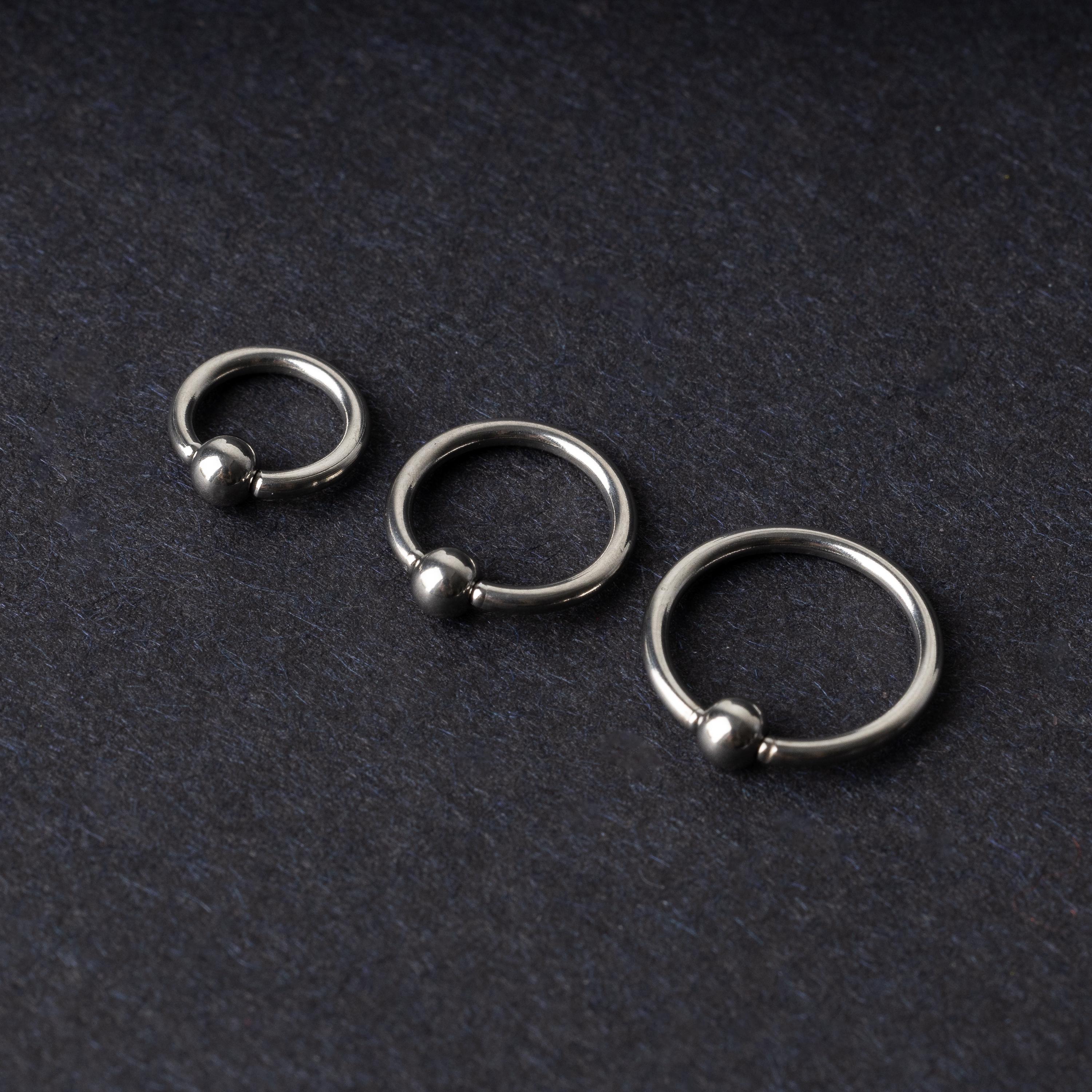 Three polished stainless steel captive bead rings of varying sizes displayed on a dark matte background.