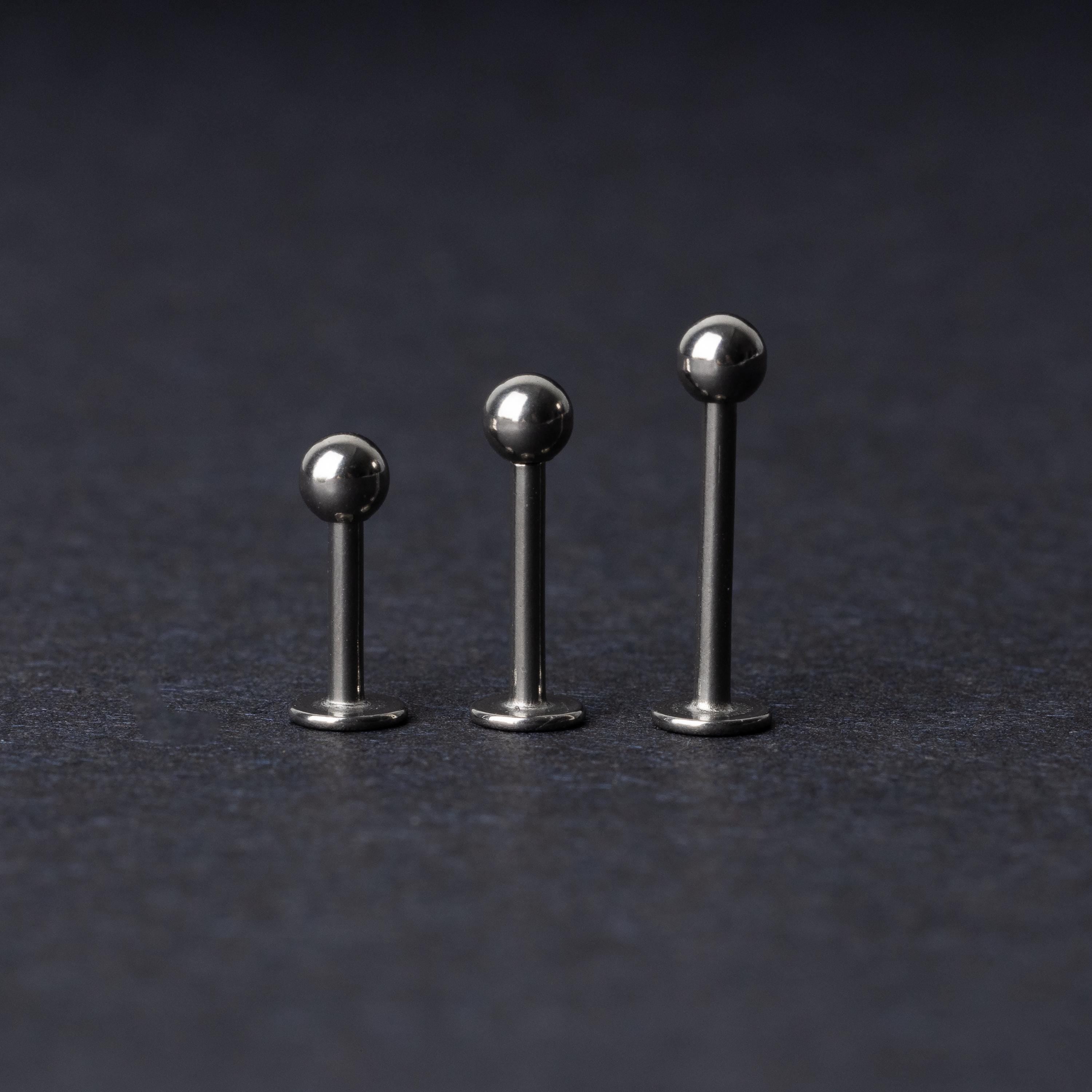 Three silver stainless steel labret studs with flat backs and polished ball ends, displayed on a dark textured background.