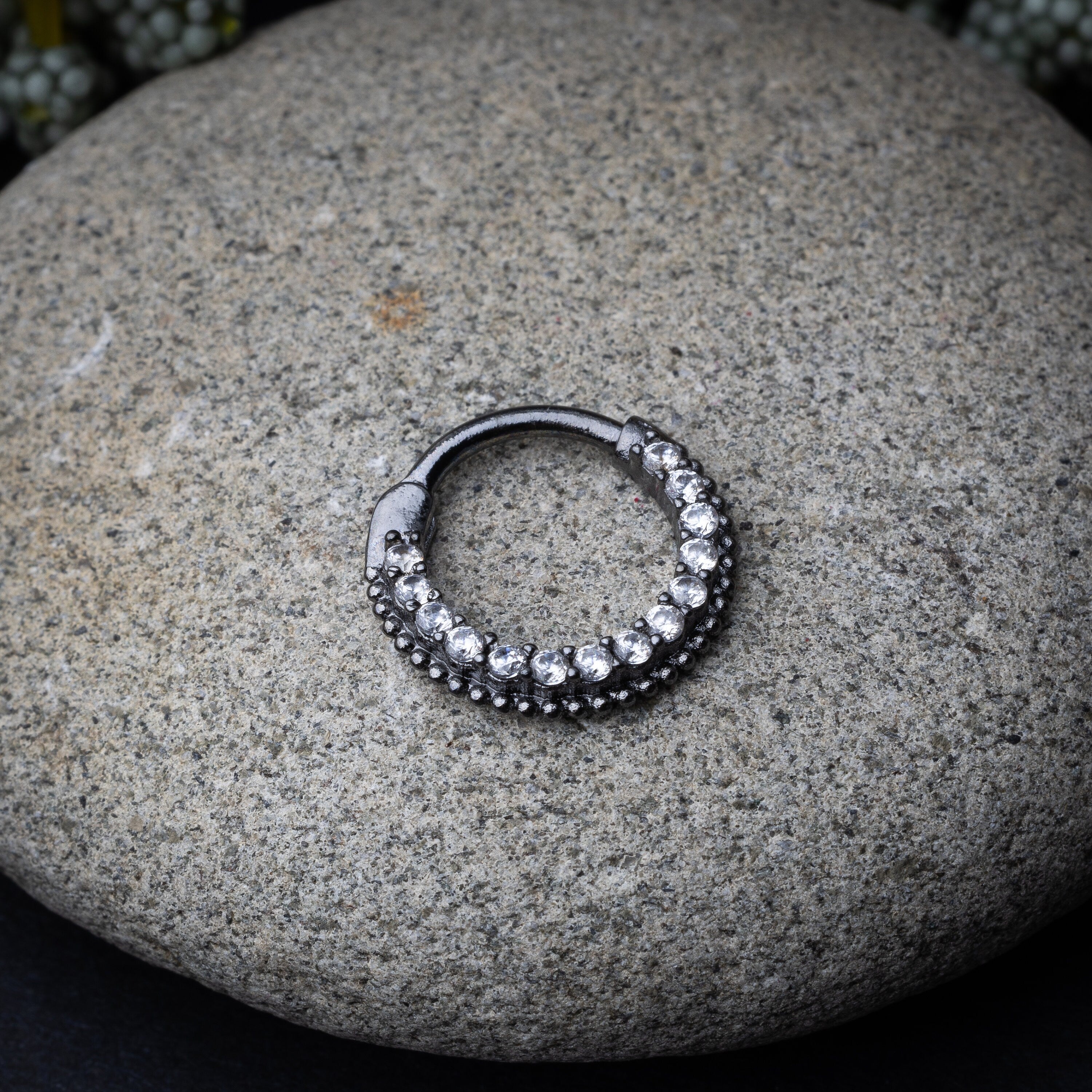 Stainless steel clicker with double rows of clear gemstones in silver displayed on a stone background