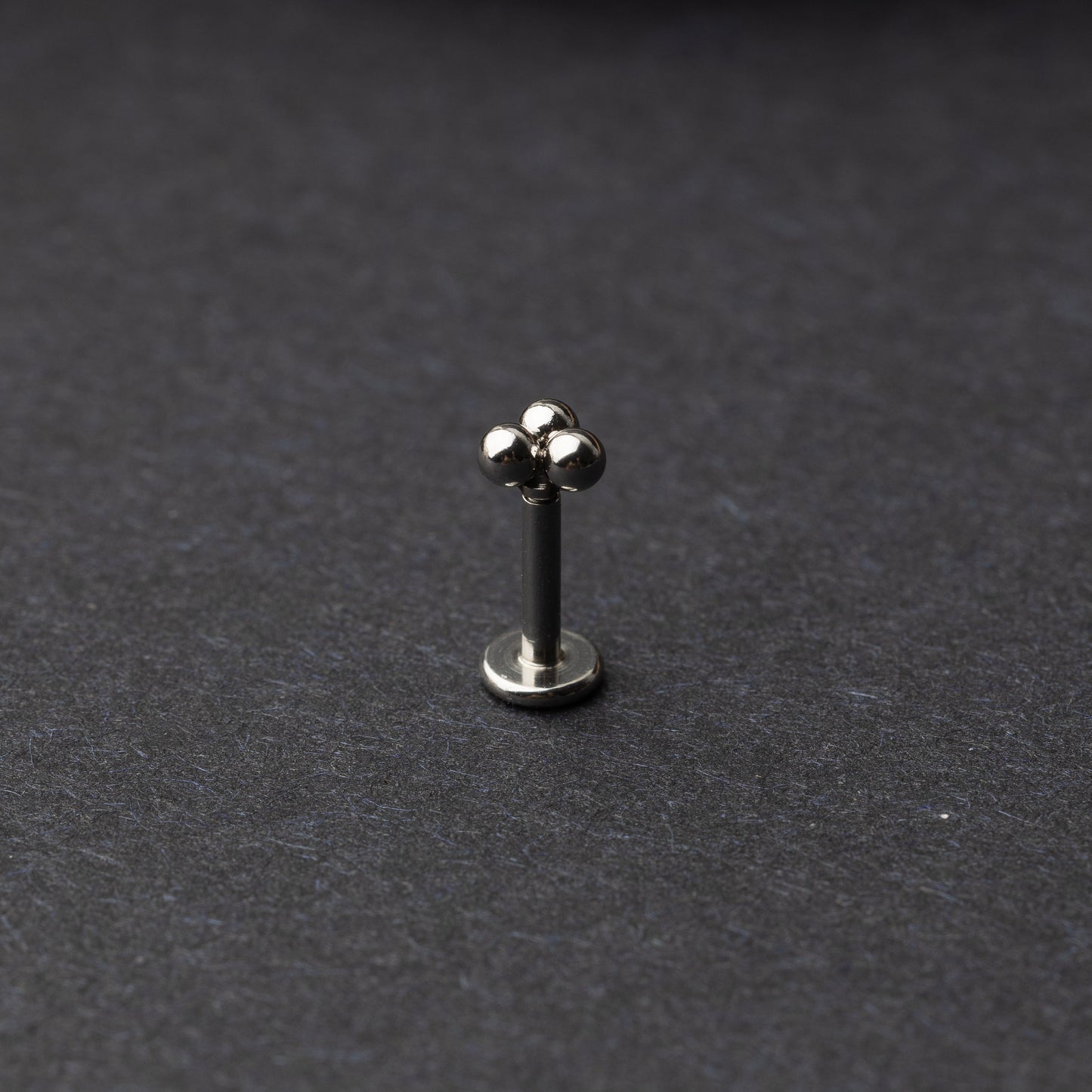 Close-up of three minimalist ball cluster labret studs in a silver finish, displayed on a dark background.