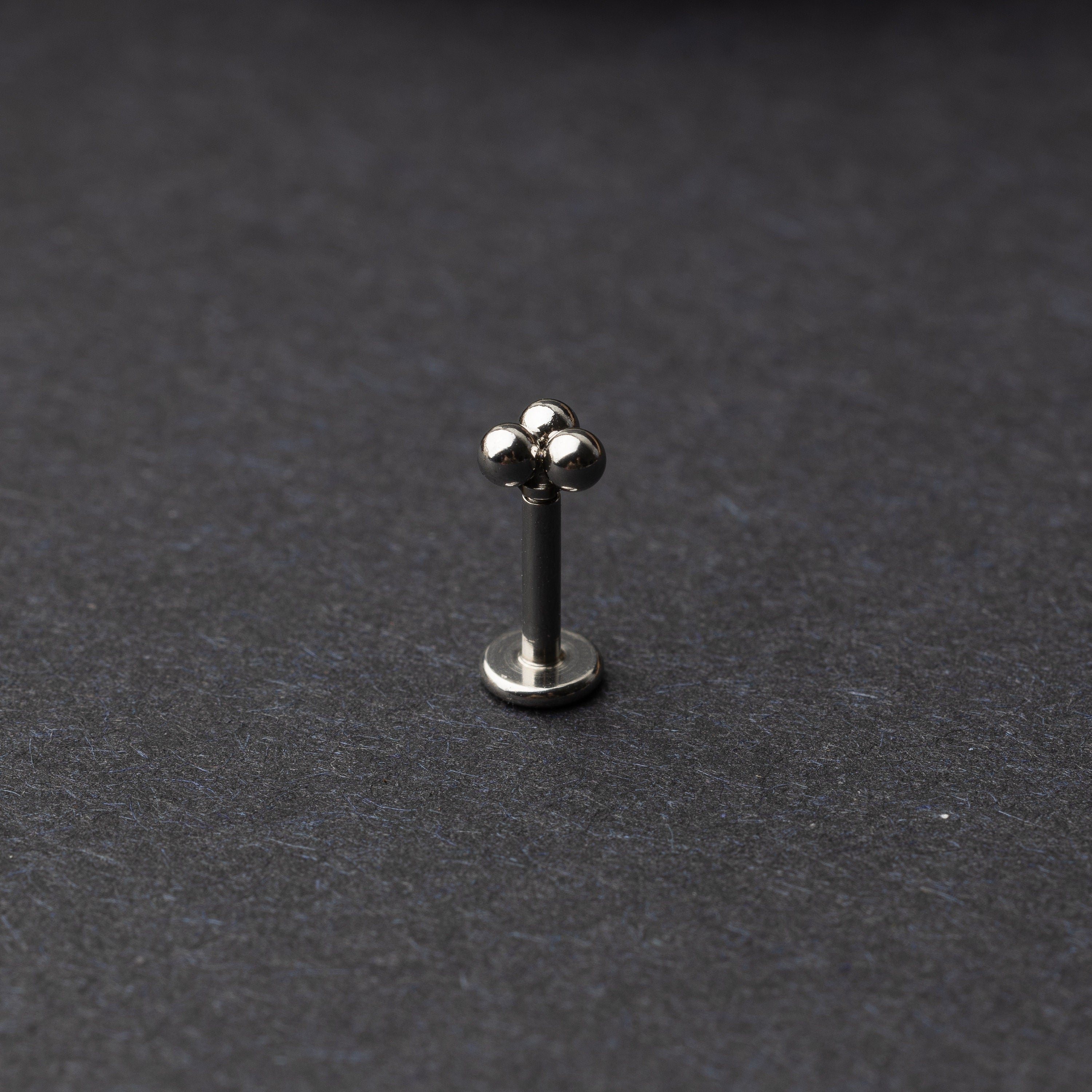 Close-up of three minimalist ball cluster labret studs in a silver finish, displayed on a dark background.