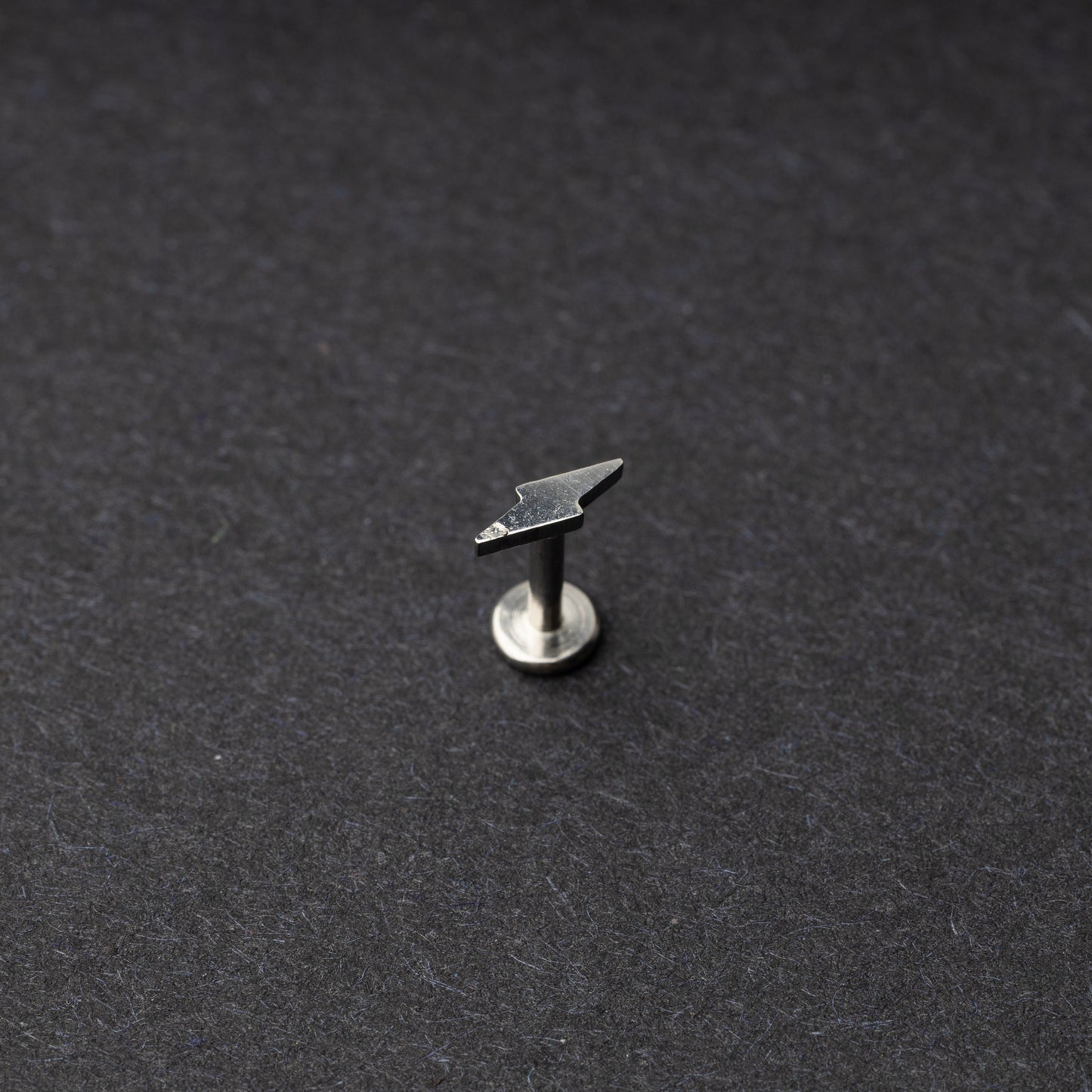 Minimalist lightning bolt labret studs in silver displayed on a dark background.