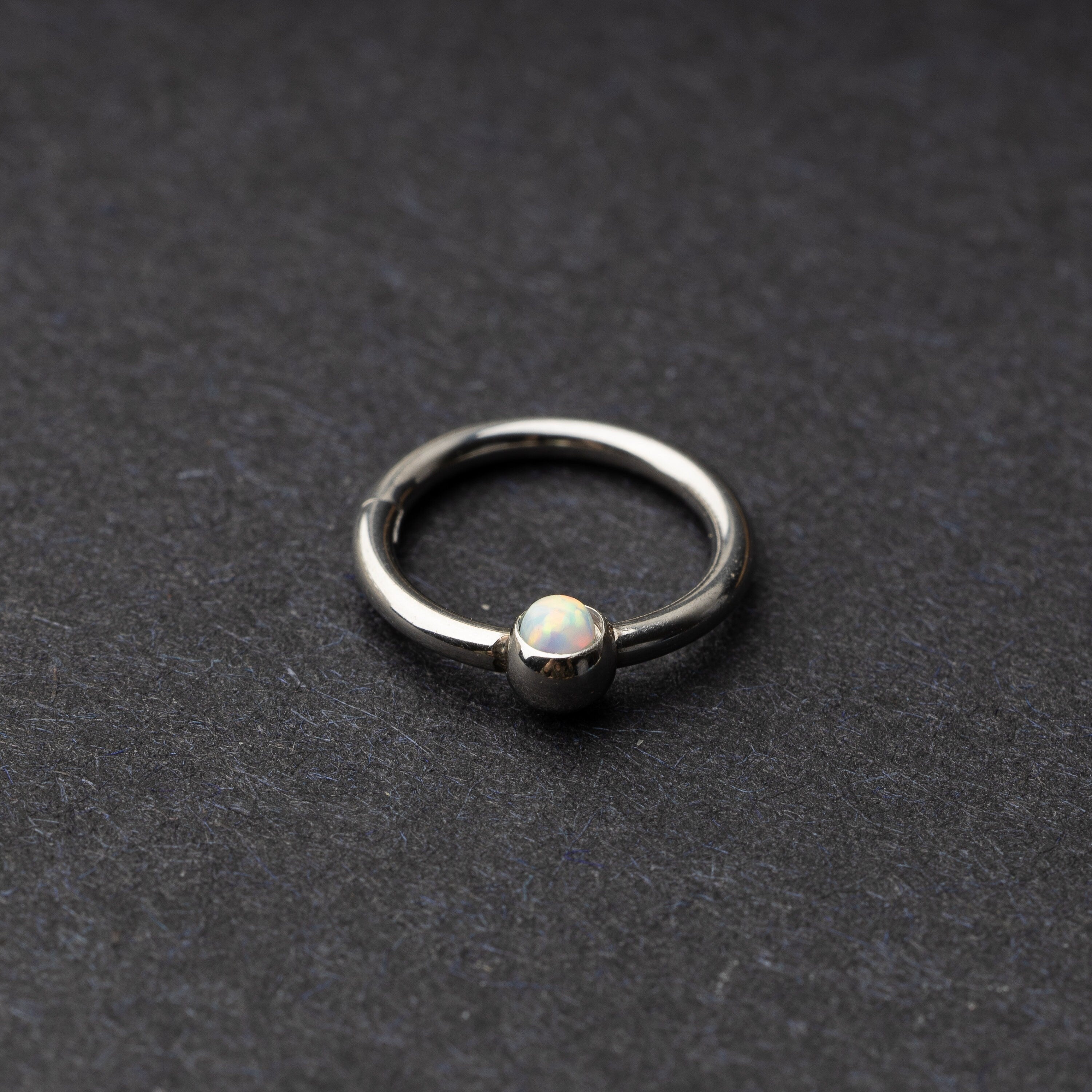 Seamless clicker in silver featuring an opalescent bead, displayed on a dark background.