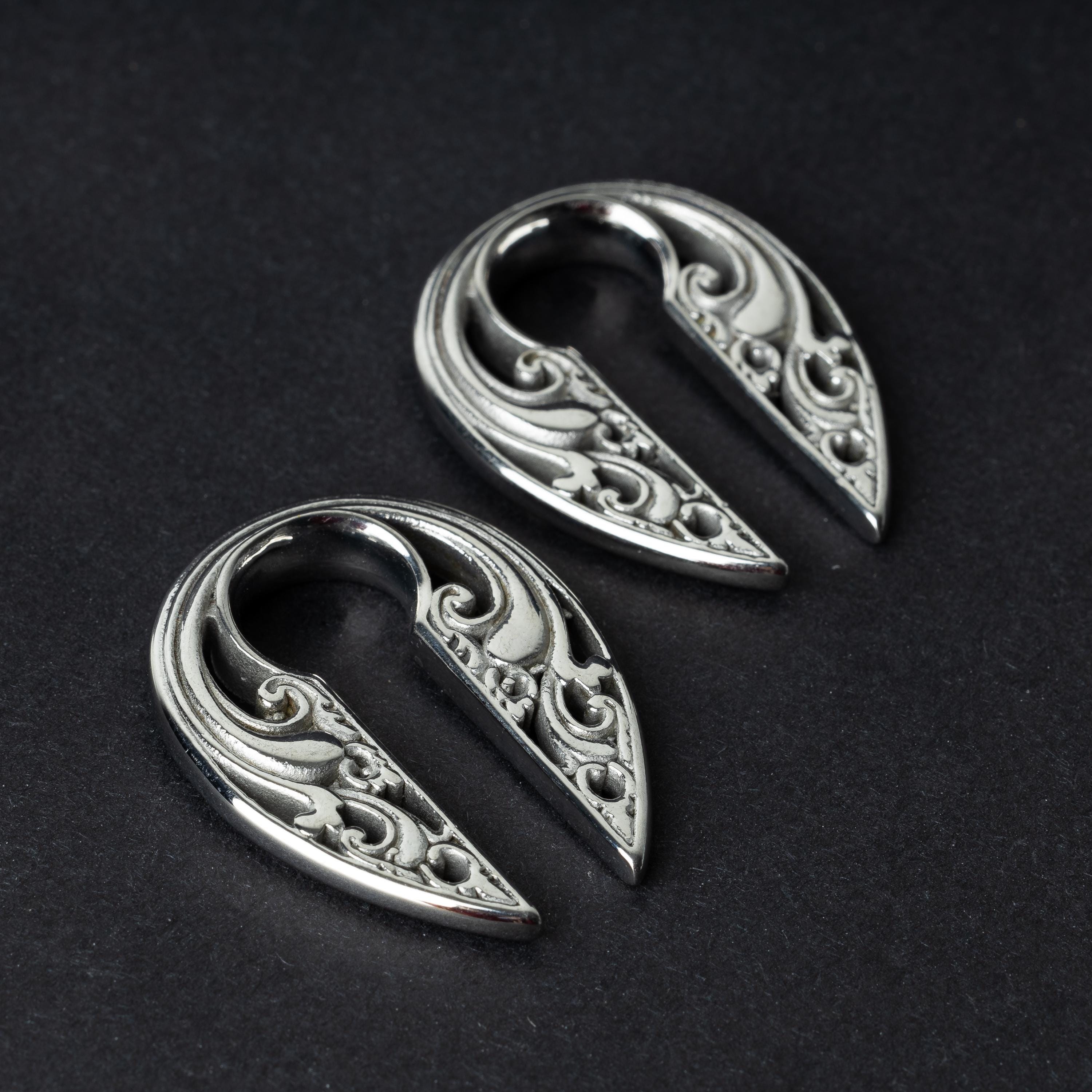 Two split ear weights with intricate filigree detailing, in polished silver, displayed on a dark background.