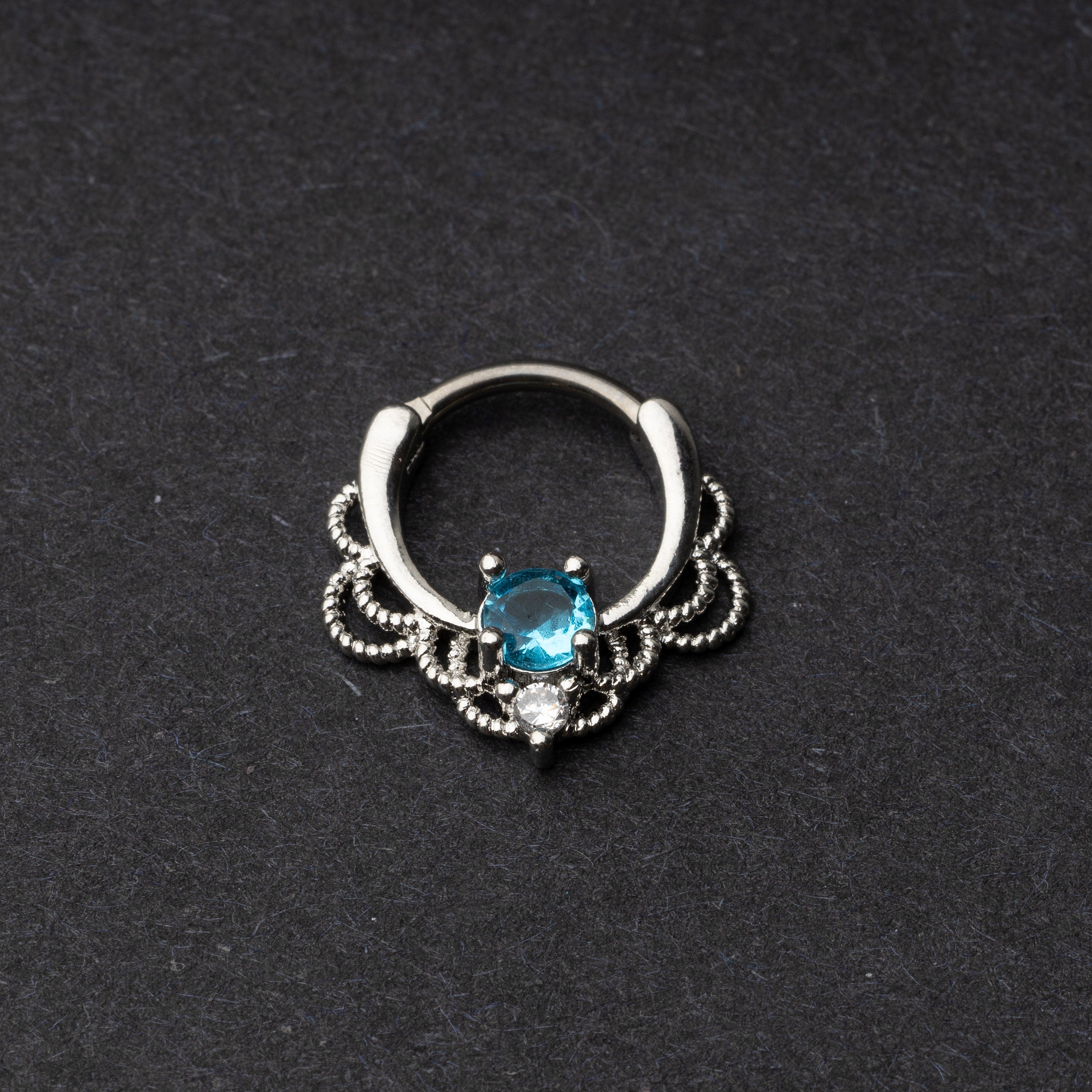 Silver Ornate Septum Ring with a Blue Gem on a dark background