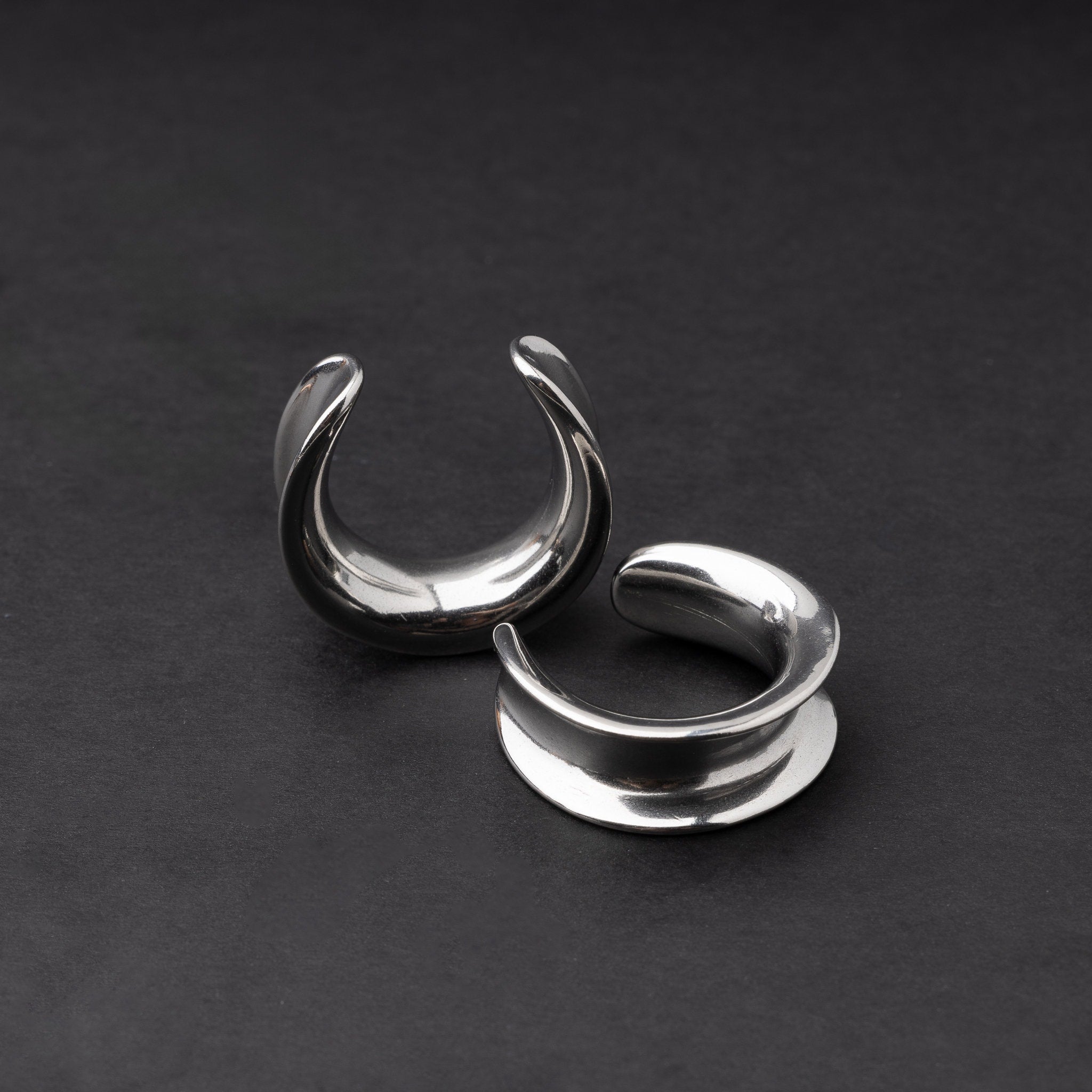 A pair of silver saddle tunnels displayed on a dark background.
