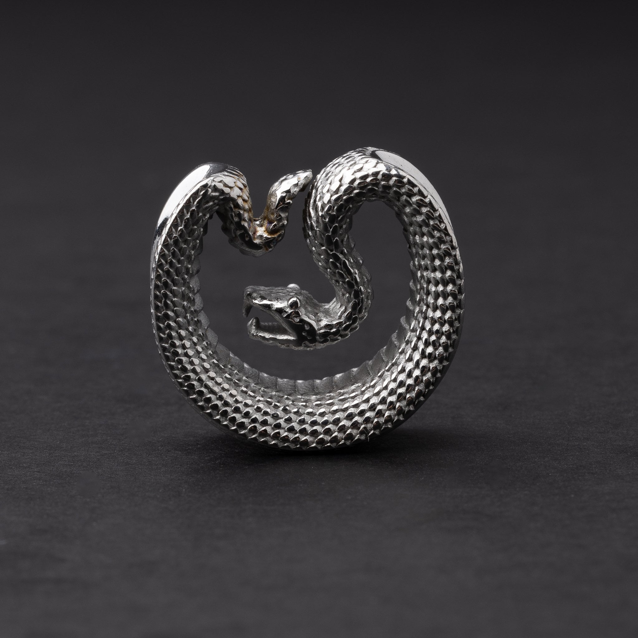 Silver Snake-shaped saddle plugs, displayed on a dark background.