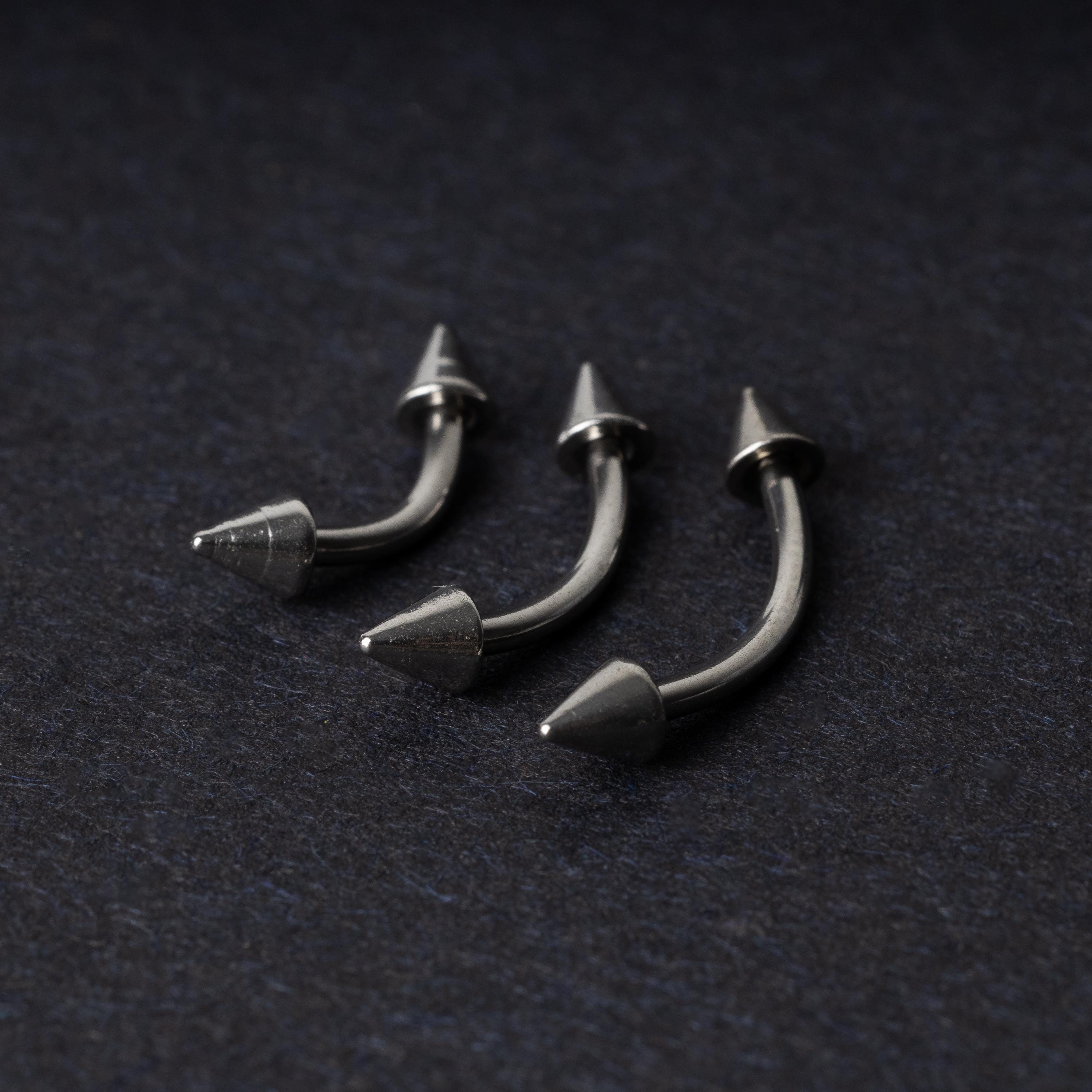 Three stainless steel curved barbells with cone-shaped ends, displayed on a dark background.