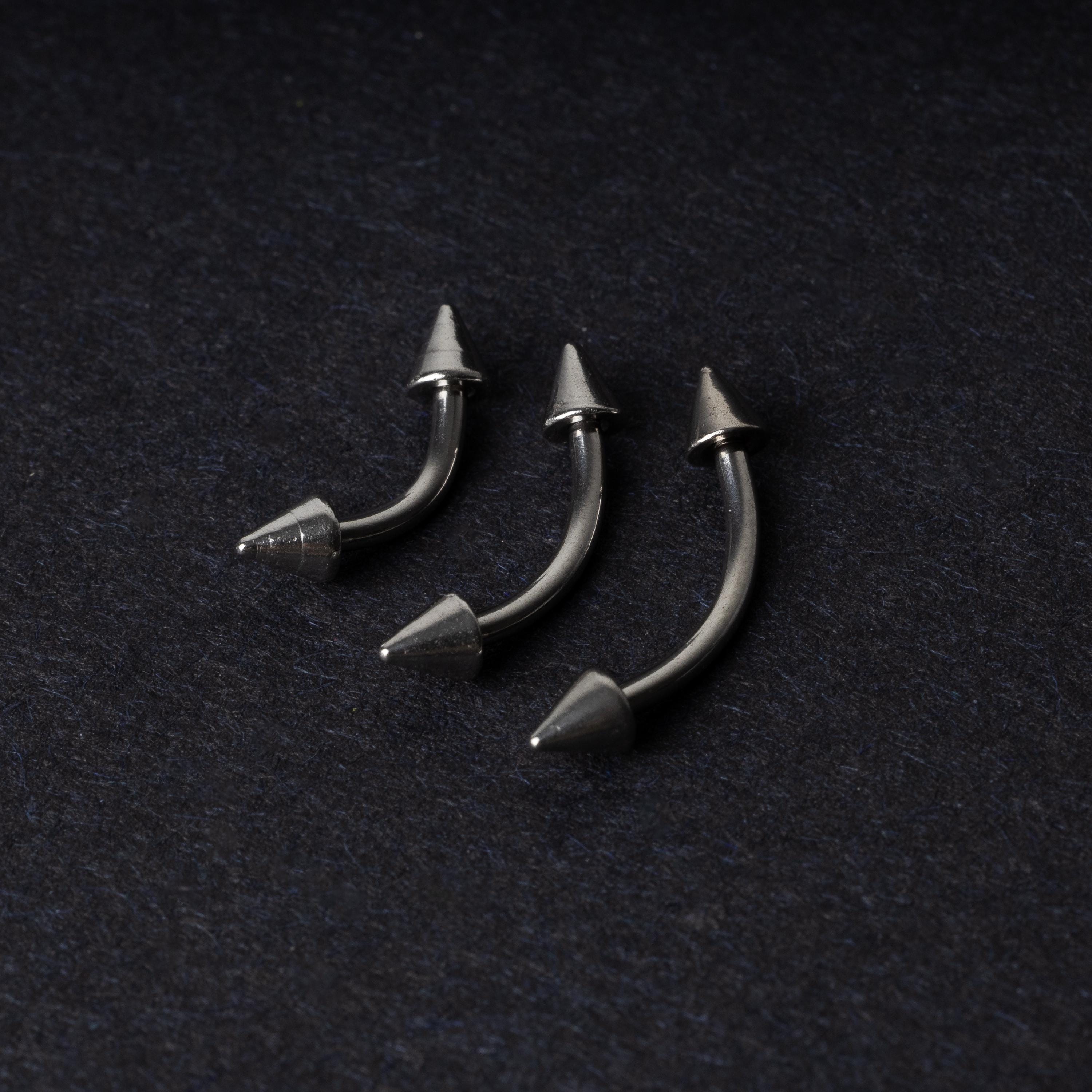 Three stainless steel curved barbells with cone-shaped ends, displayed on a dark background.
