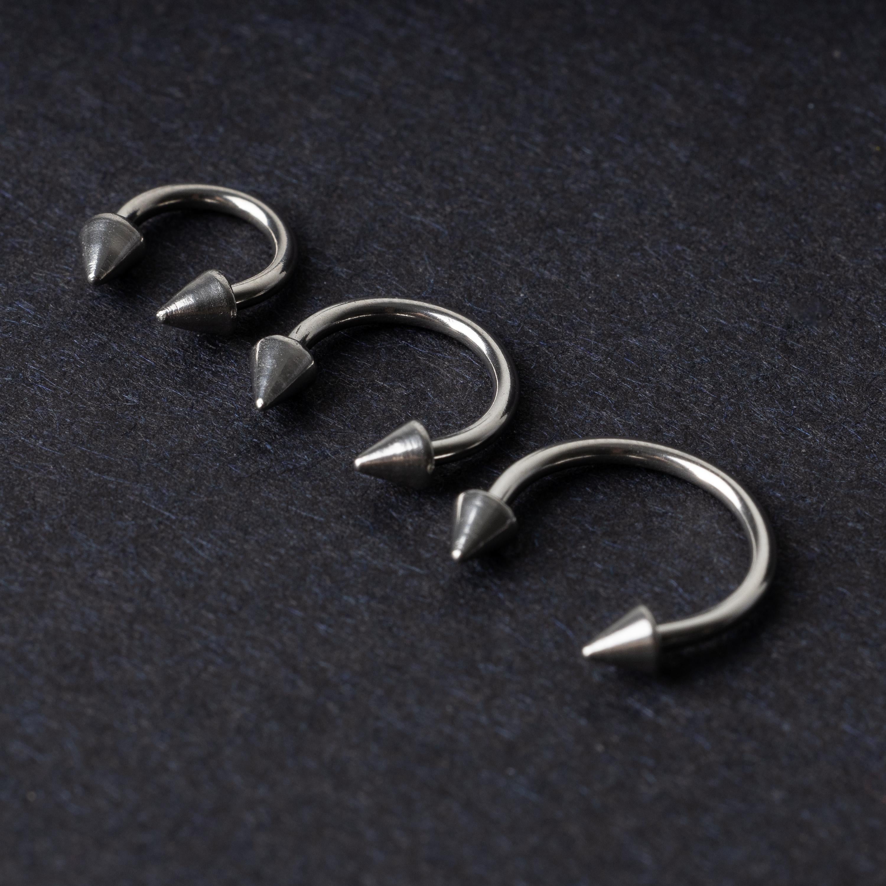 Three stainless steel horseshoe hoops with cone-shaped ends, arranged on a dark background.